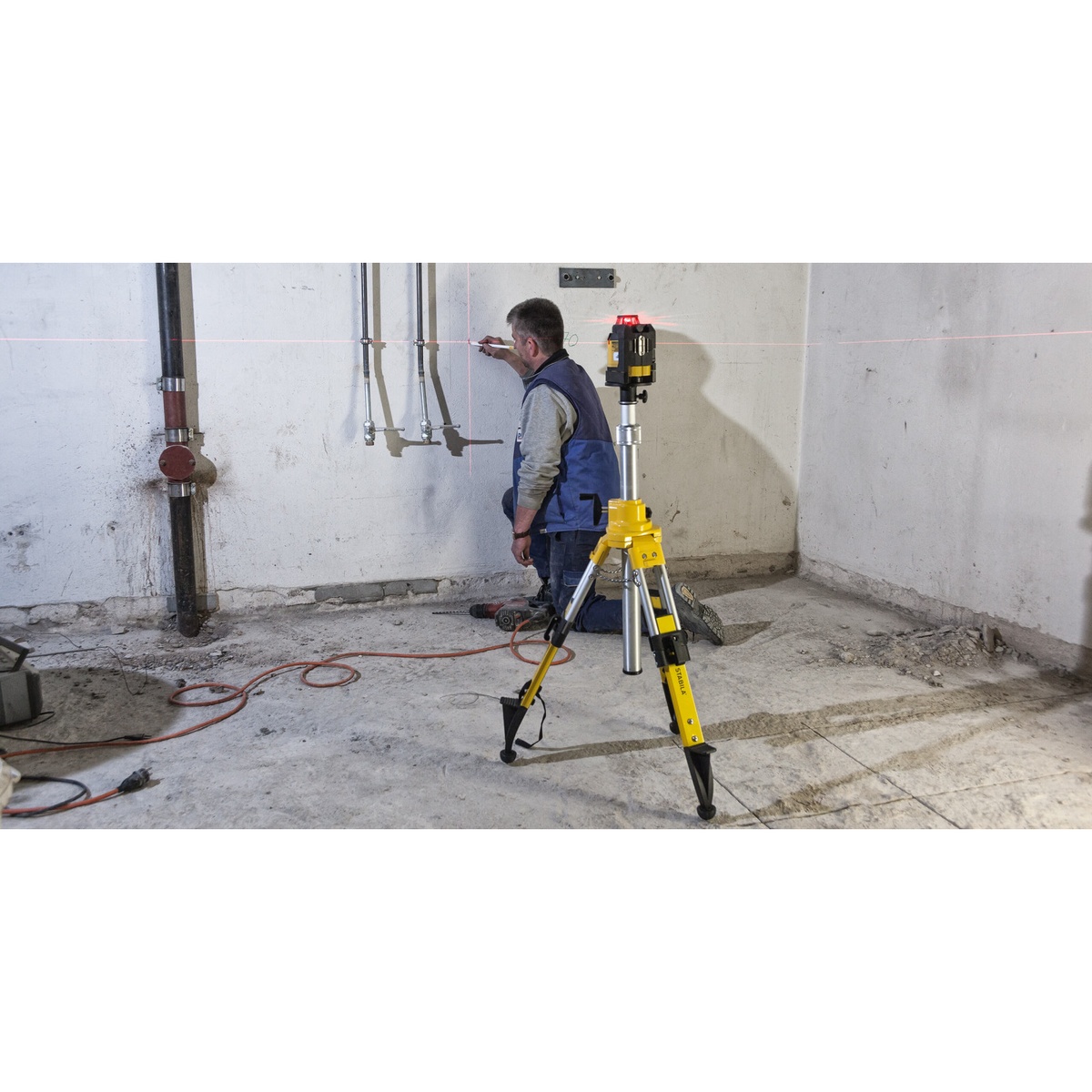 Stabila 08560 tripod with mounted laser level projecting a horizontal line across a rough interior room during installation work