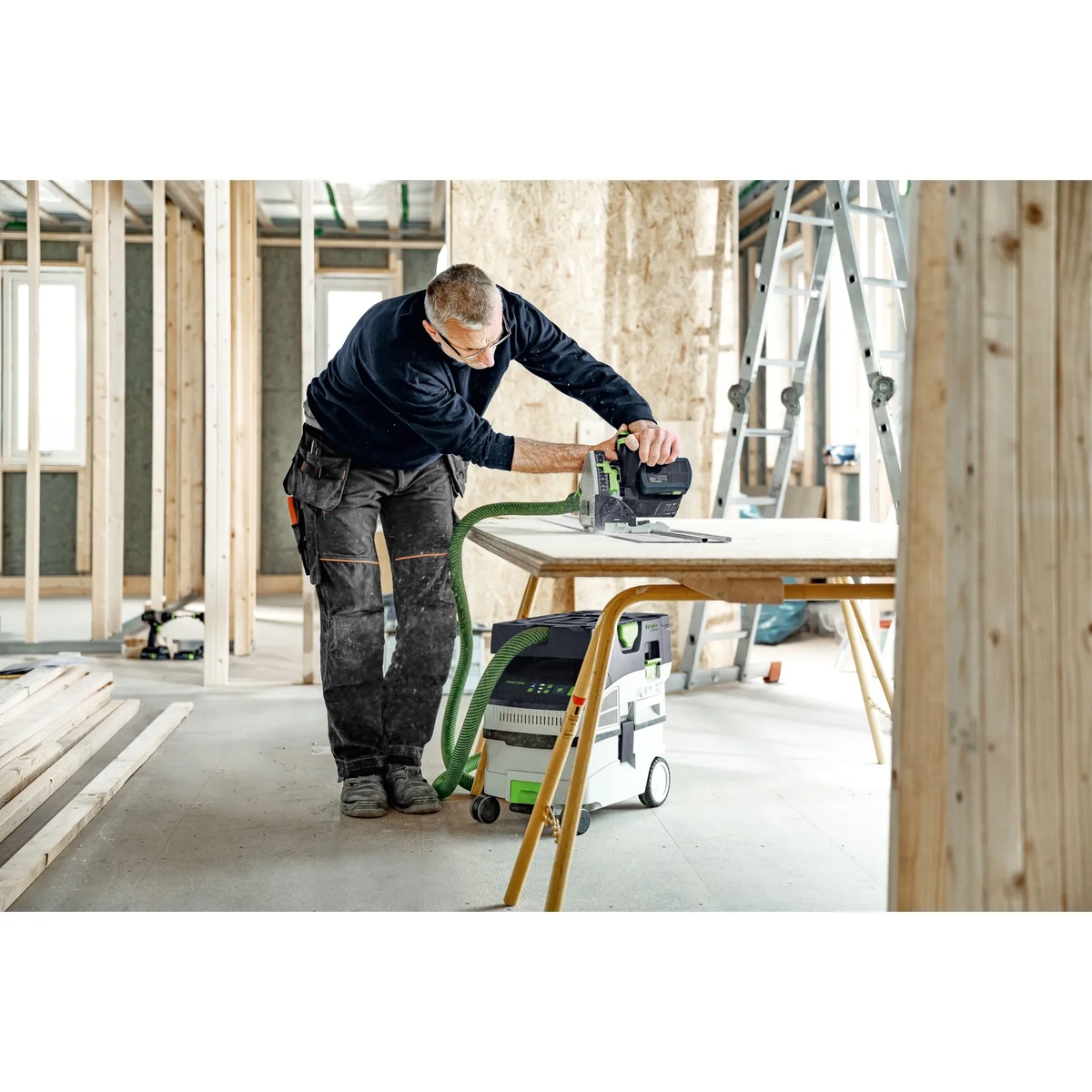 Festool 577069 CLEANTEC CTC MIDI I HEPA-Basic Cordless Mobile Dust Extractor collecting dust from a cordless saw during interior sheet cutting on a framing jobsite
