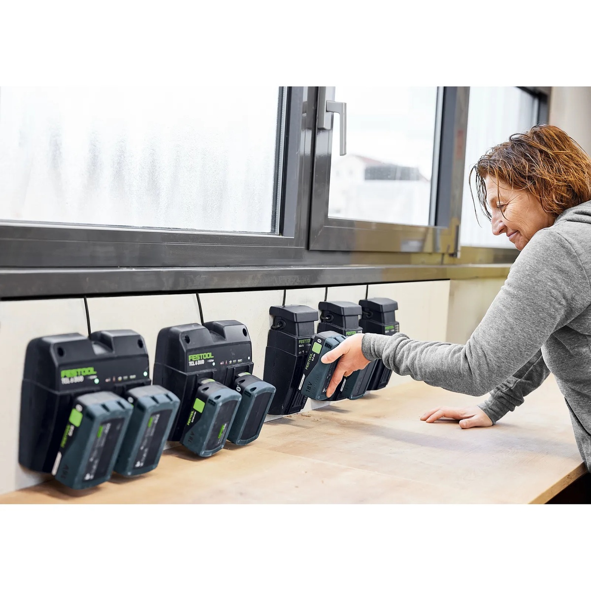 Festool 577079 Energy Set SYS 18V 2x5.0/TCL 6 DUO battery pack being placed on a wall-mounted charger in a workshop charging station