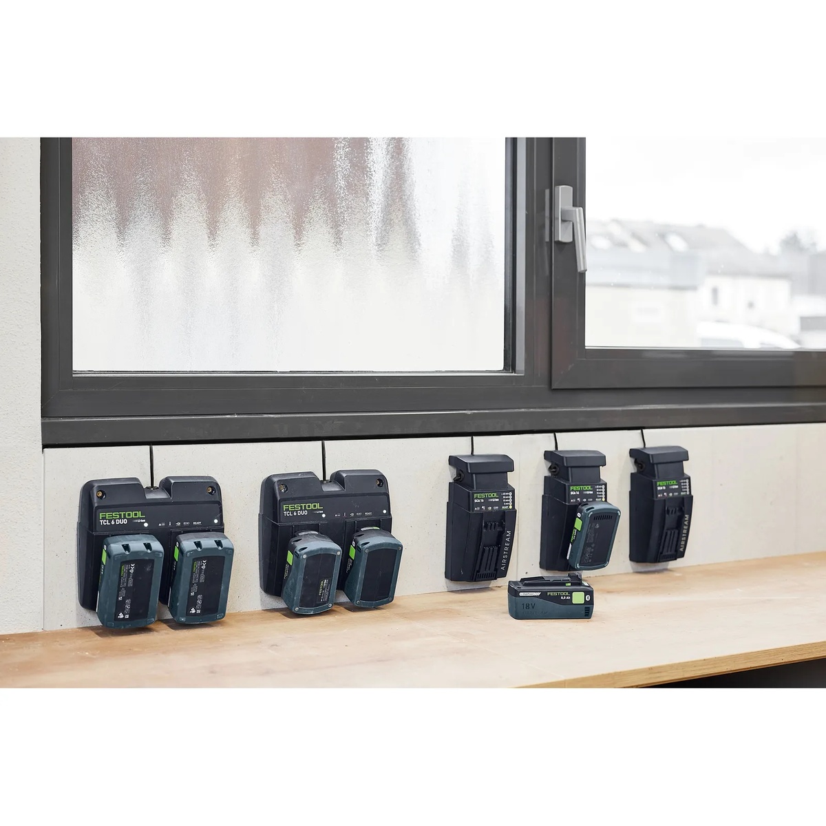 Festool battery chargers and 18 volt battery packs arranged along a workshop bench to show system charging and organized cordless power storage