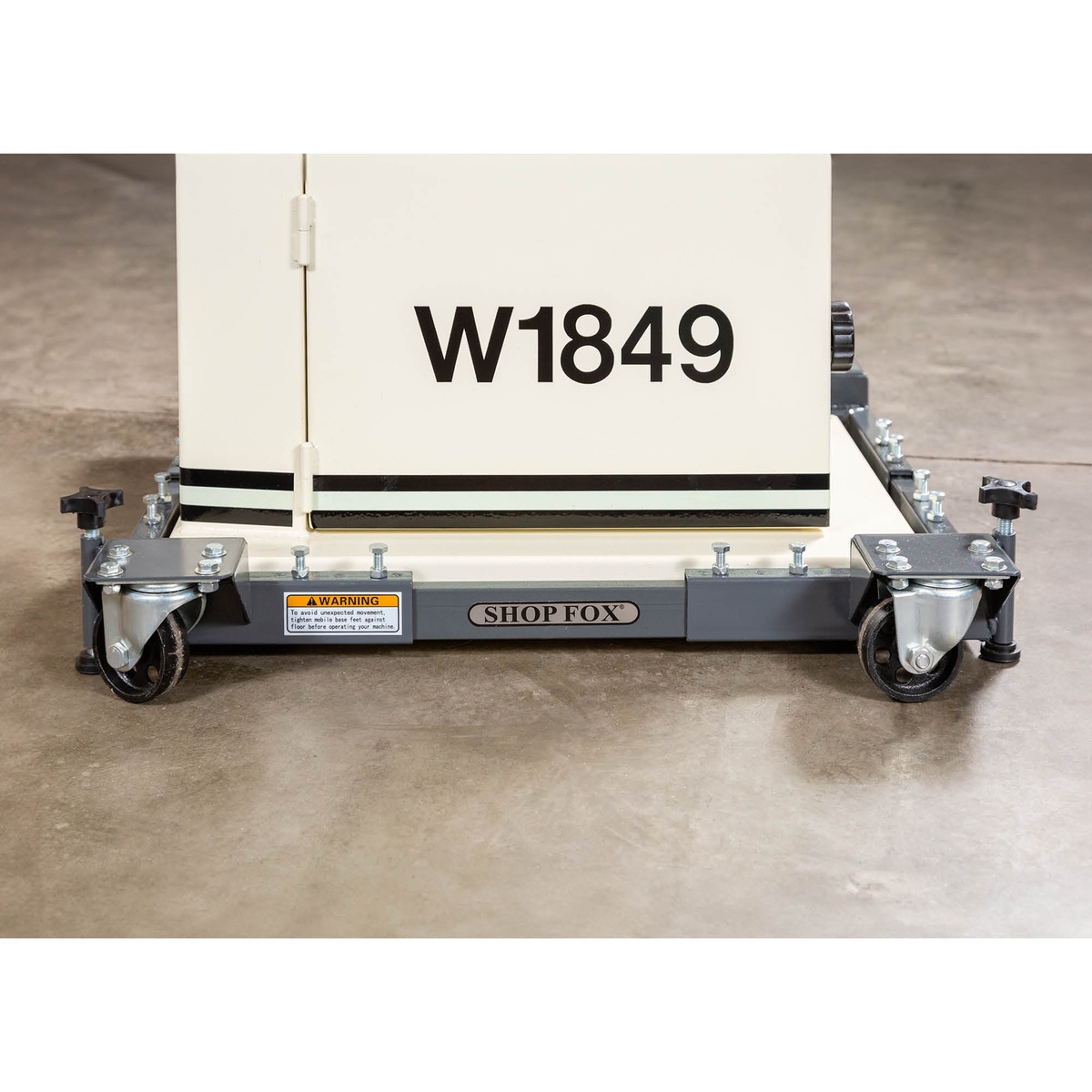 Shop Fox D2058A Adjustable Mobile Base supporting a stationary woodworking machine on a concrete shop floor for machine mobility in a small workshop