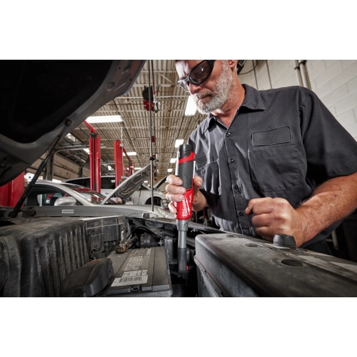 Milwaukee M12 FUEL 1/4 inch Extended Reach High Speed Ratchet removing or installing hardware in an automotive shop during battery area service