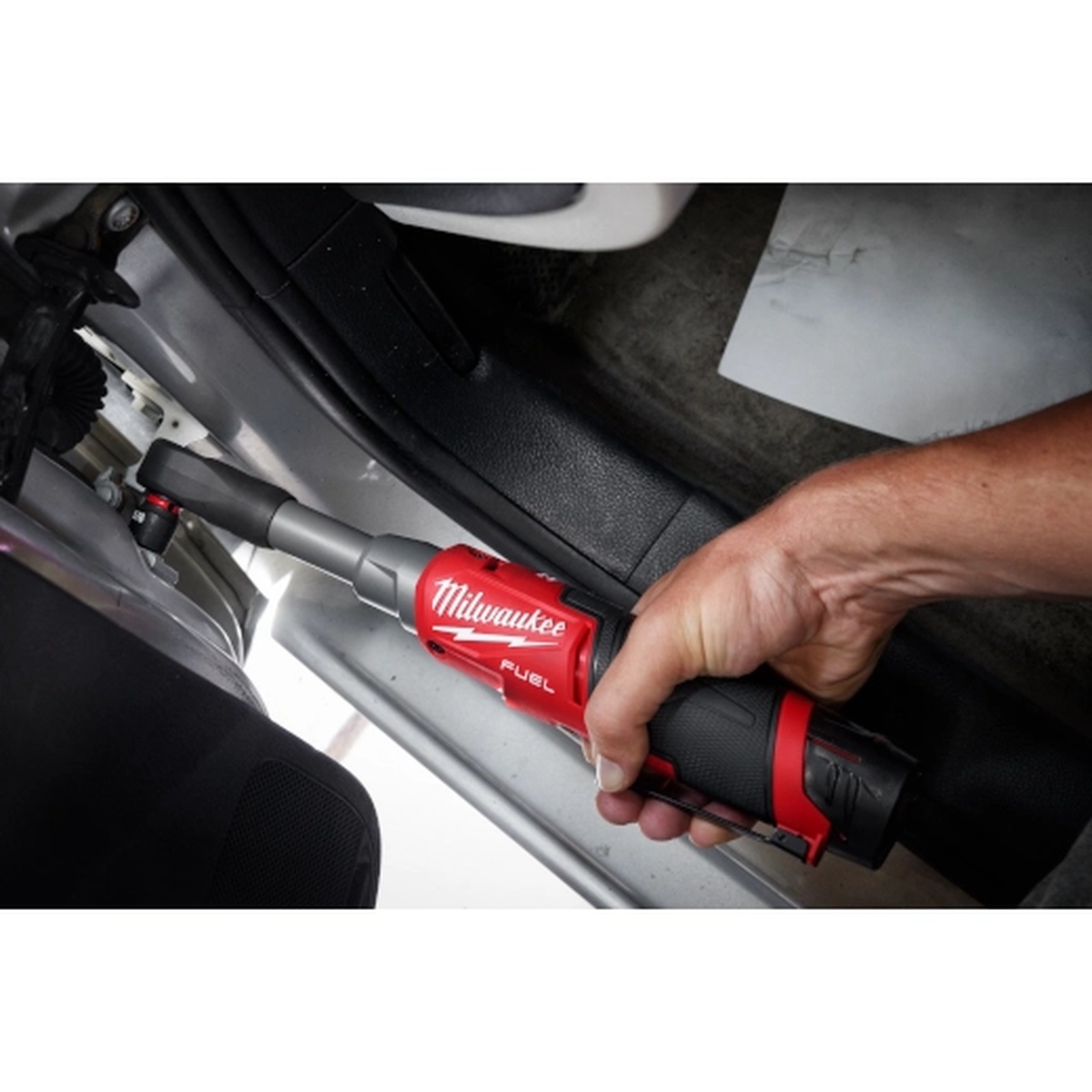 Milwaukee M12 FUEL 1/4 inch Extended Reach High Speed Ratchet working on a door sill fastener inside a vehicle cabin during interior automotive repair