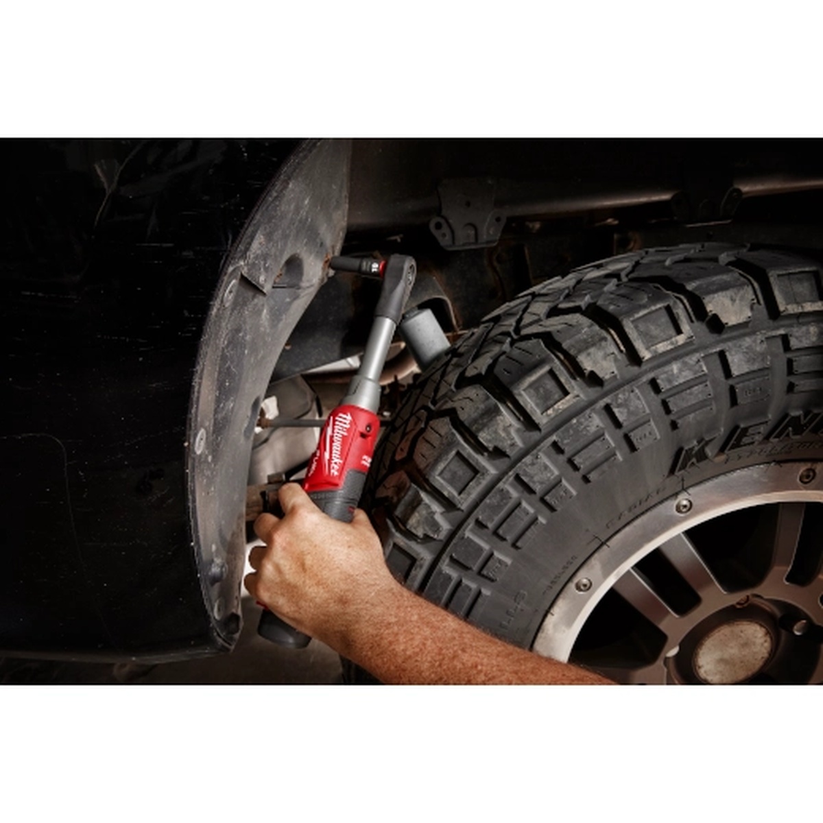 Milwaukee M12 FUEL 3/8 in Extended Reach High Speed Ratchet removing a fastener inside a wheel well on a lifted truck, showing long reach around suspension and tire clearance