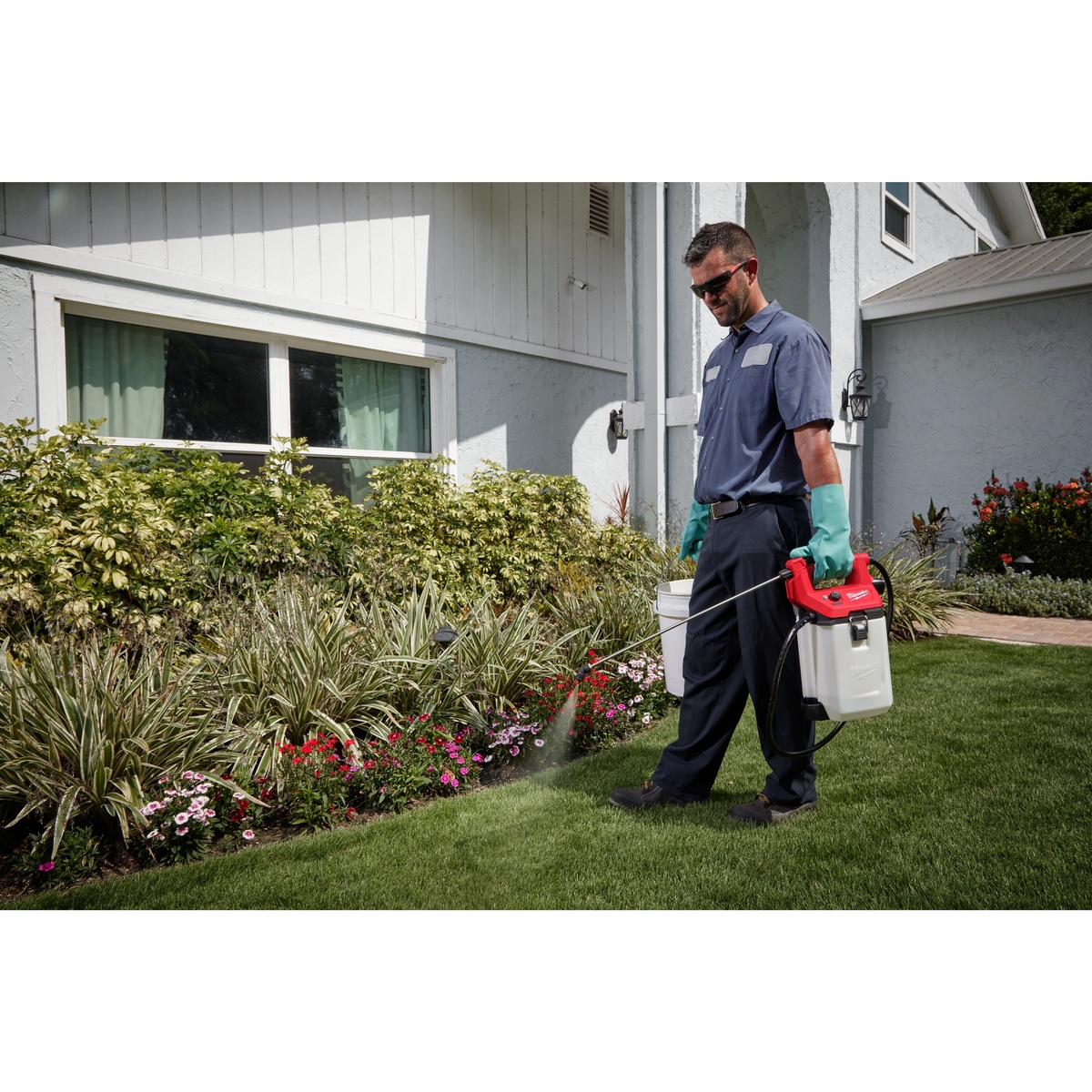 Milwaukee M12 2 Gallon Handheld Sprayer Kit being used for lawn and landscape spraying around a residential flower bed