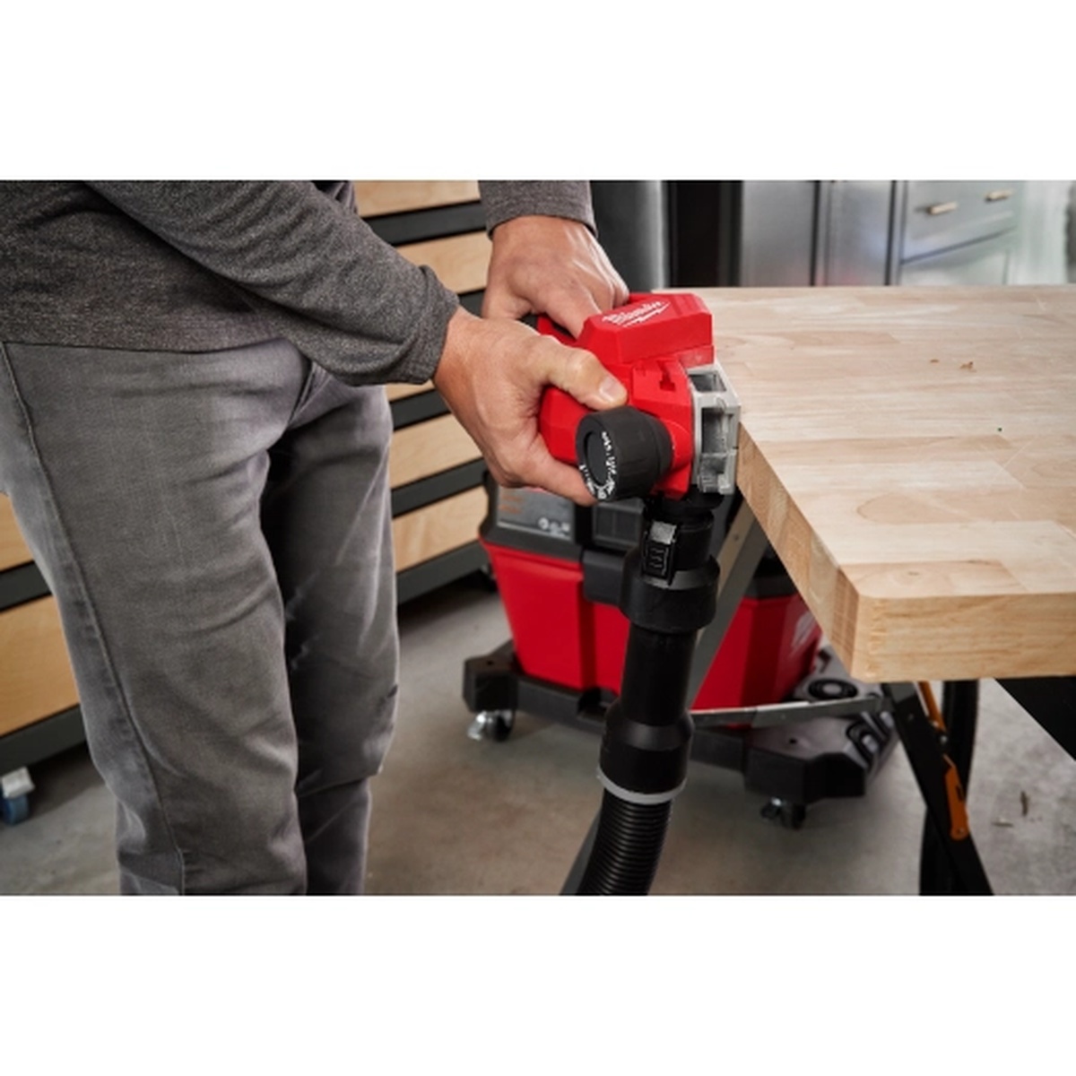 Milwaukee M12 Brushless 2 inch Planer in use on a wood workbench edge with a vacuum attached during finish carpentry work in a shop
