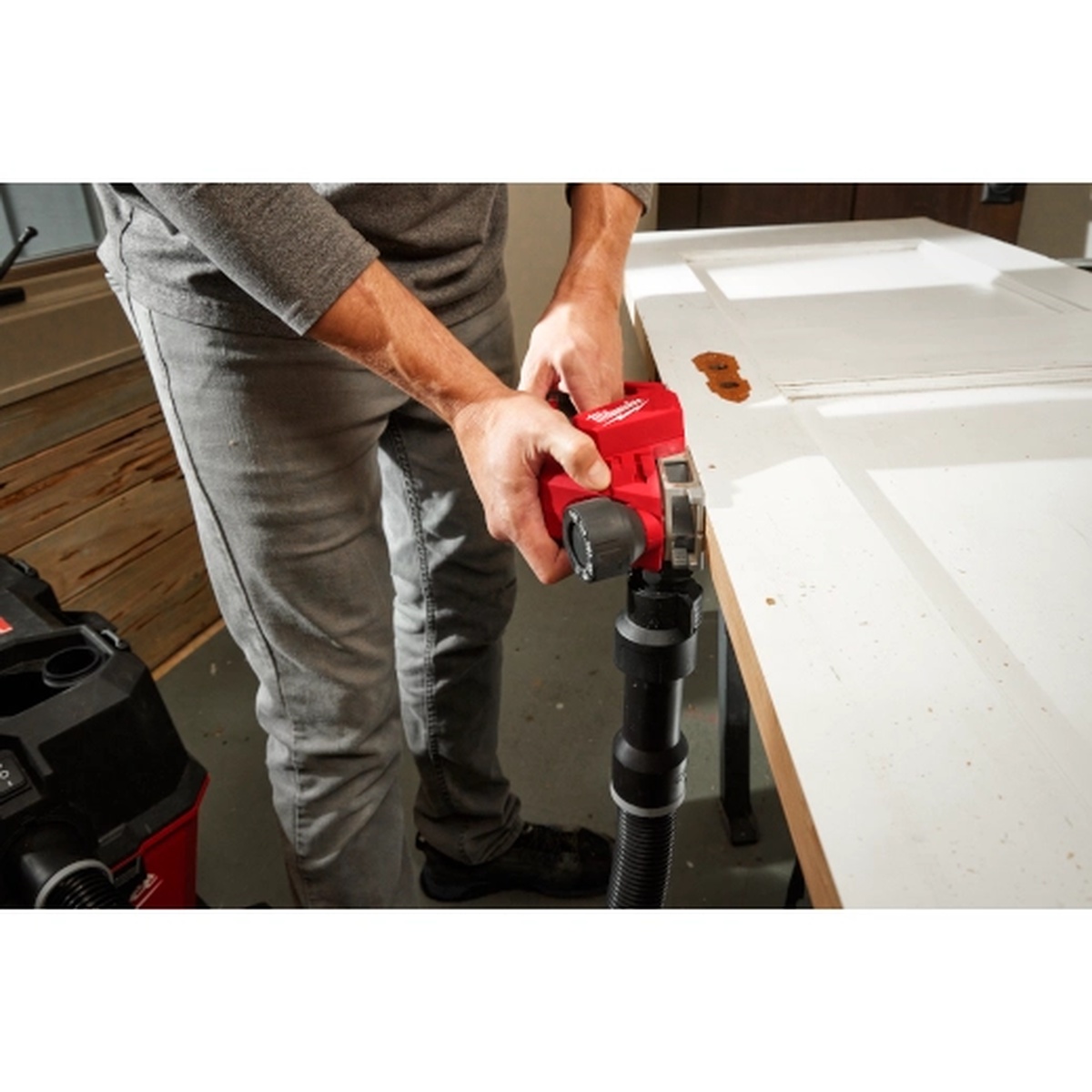Milwaukee M12 Brushless 2 inch Planer trimming the edge of a painted interior door with a vacuum hose attached during remodeling work
