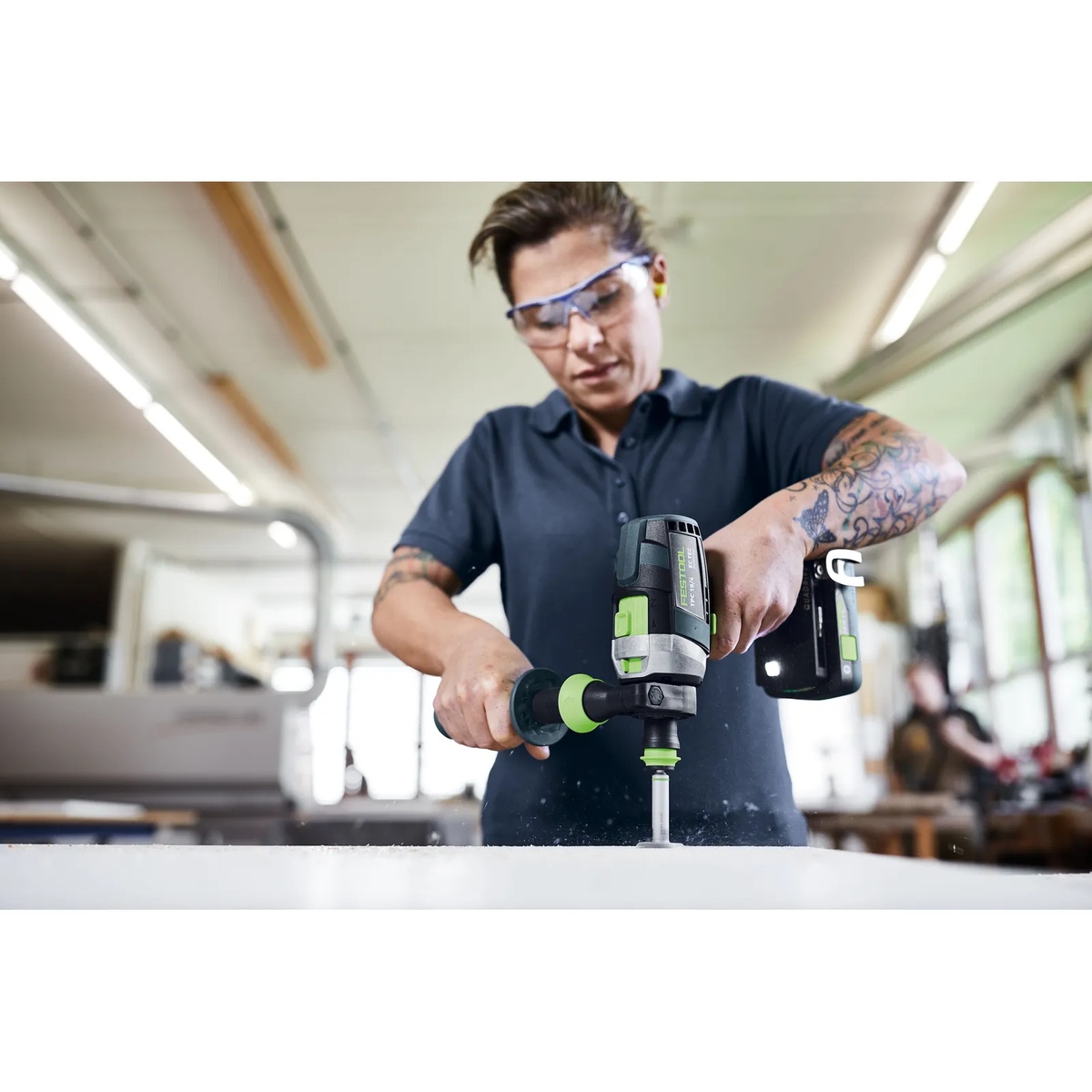 Festool 577627 QUADRIVE TPC 18/4 Cordless Hammer Drill driving a fastener into a work surface with the side handle installed in a workshop