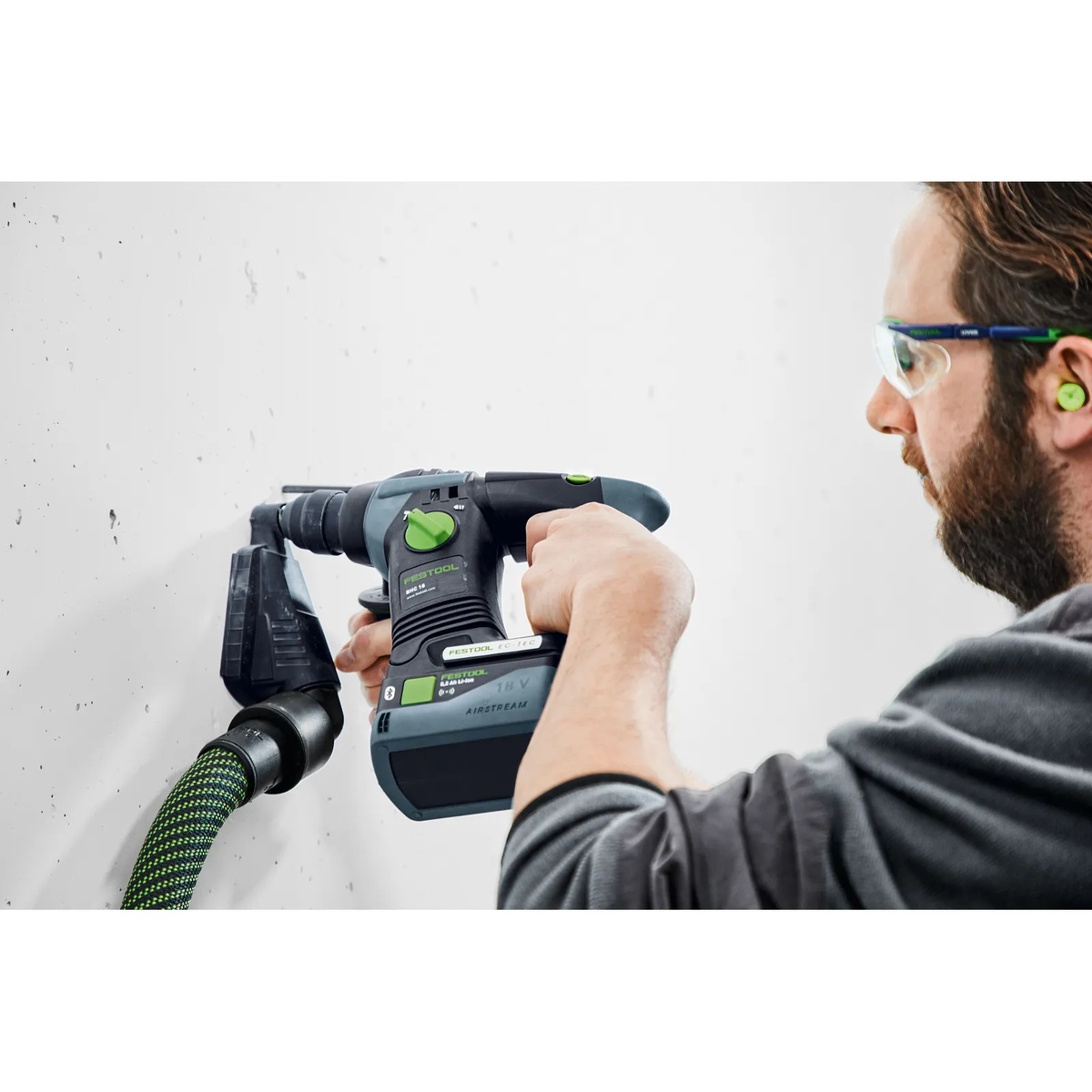 Festool BP 18 Li 5,0 ASI Battery Pack installed on a Festool cordless rotary hammer while drilling concrete with dust extraction connected on a jobsite wall