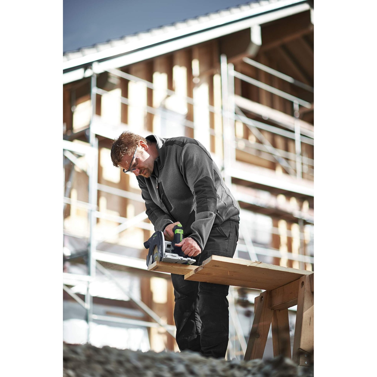 Festool HKC 55 cordless track saw making a crosscut on a jobsite wood plank at a building site