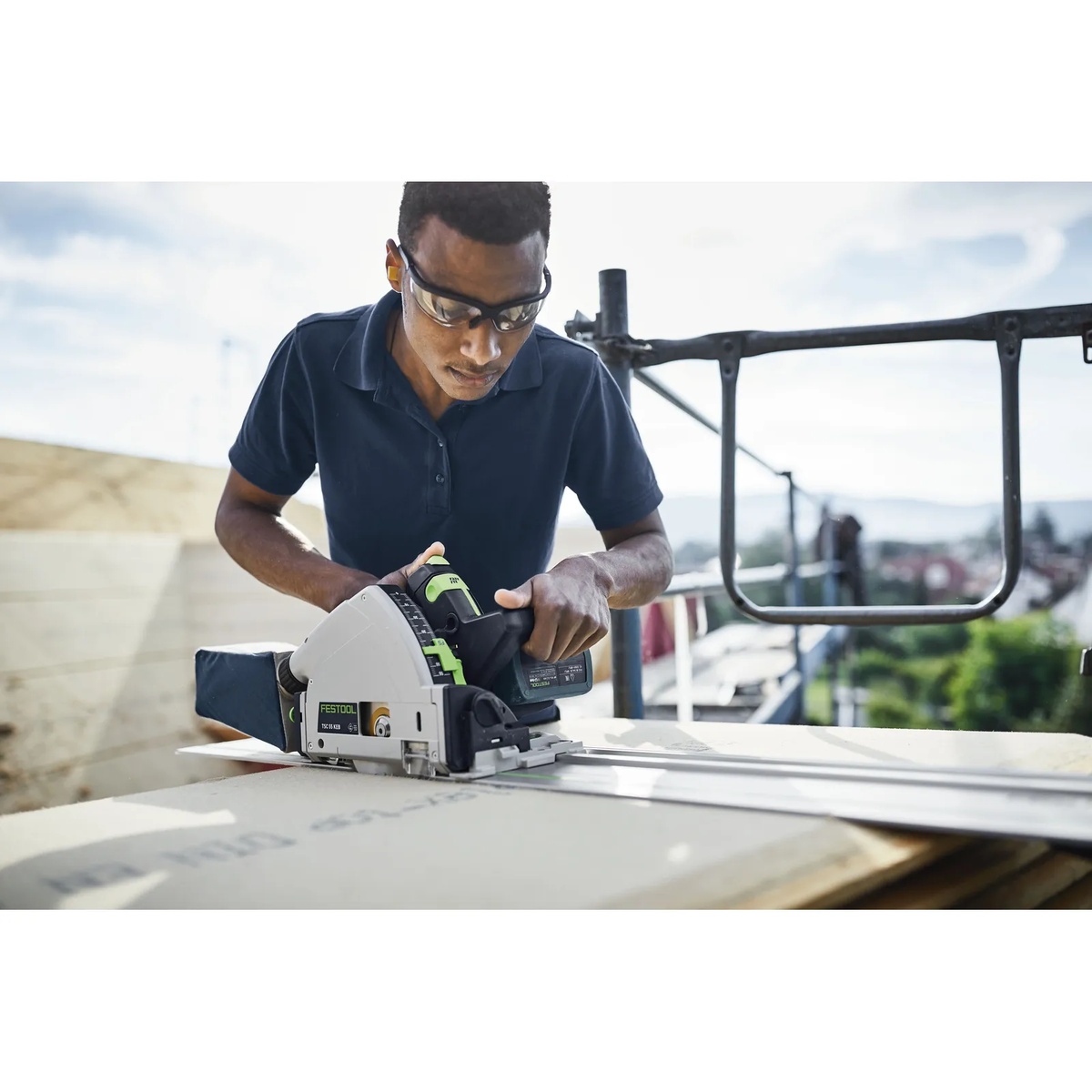 Festool 577677 TSC 55 K Cordless Track Saw 5.0Ah Kit with Kickback Stop cutting sheet material on a guide rail at an outdoor jobsite