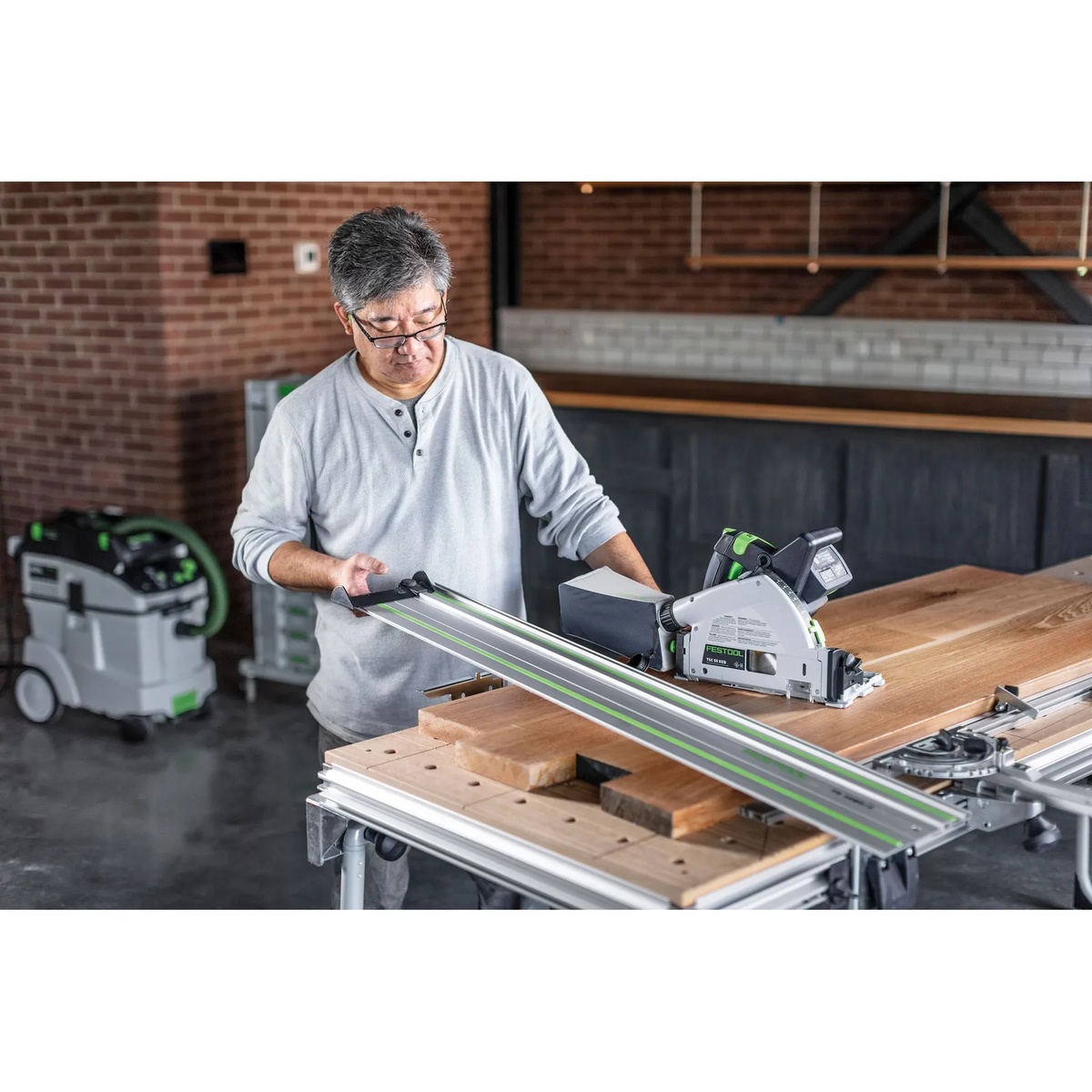 Festool 577677 TSC 55 K Cordless Track Saw 5.0Ah Kit with Kickback Stop making a guided cut across a hardwood workpiece on a workbench in a woodworking shop