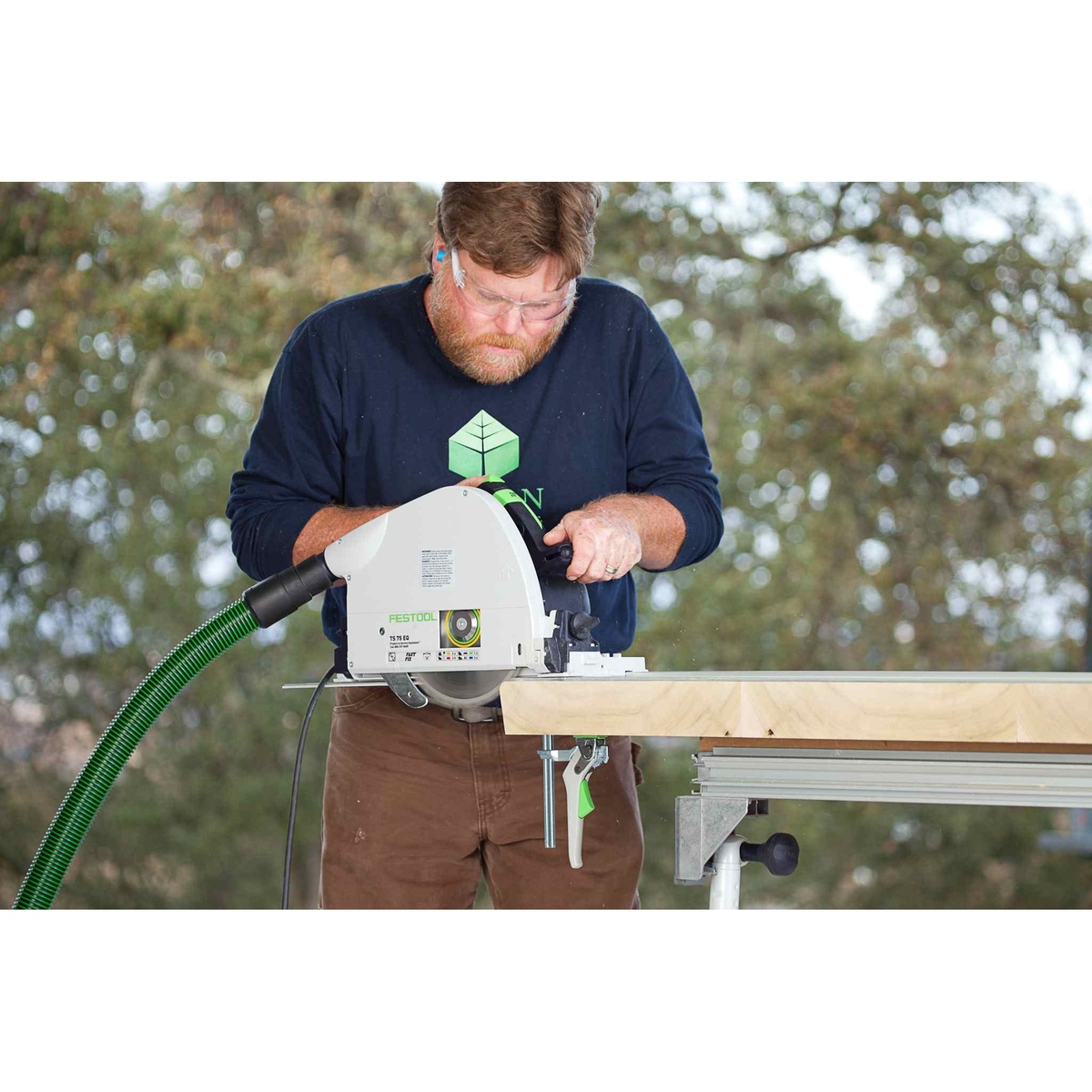 Festool TS 75 EQ Plunge Cut Track Saw making a guided cut through thick wood on a portable work table outdoors