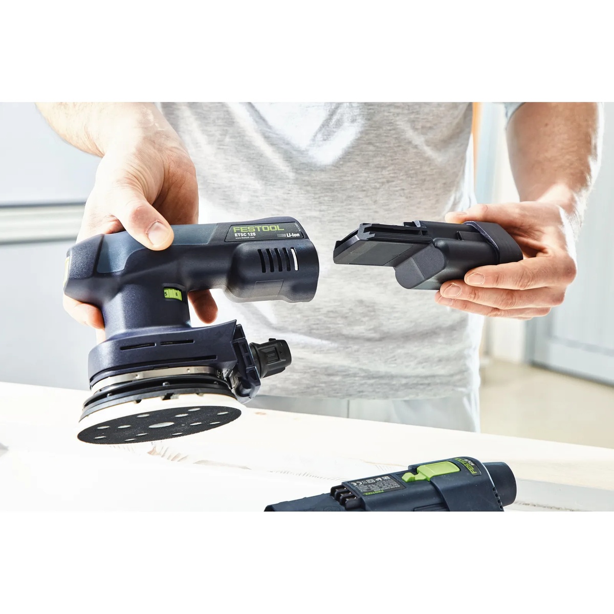 Festool ETSC 125 3,0 I-Plus US cordless random orbit sander being fitted with its Ergo battery during finish sanding setup at a workbench