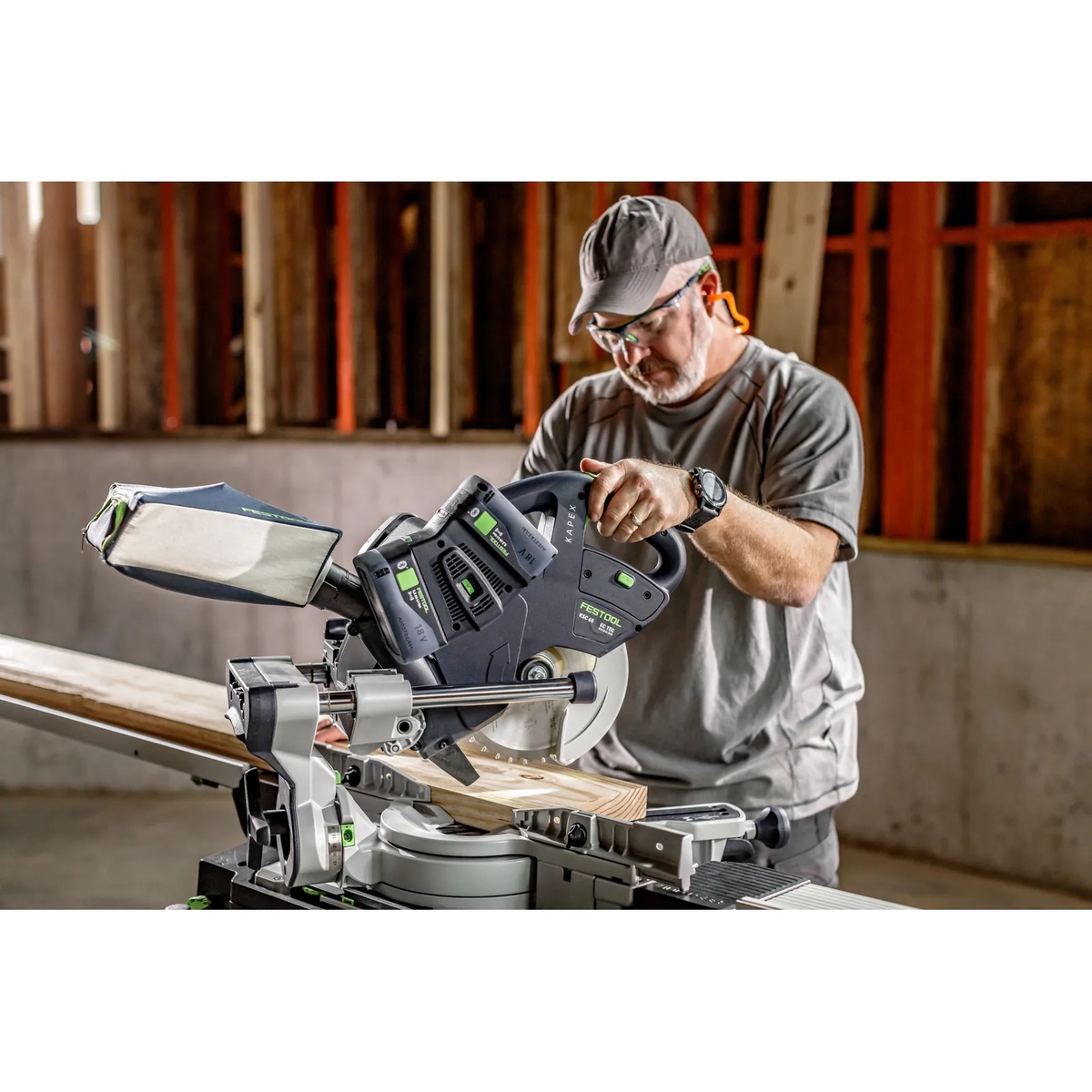 Festool KAPEX KSC 60 EB-Basic Sliding Compound Miter Saw cutting framing lumber on a jobsite work surface with dual batteries installed and dust bag attached