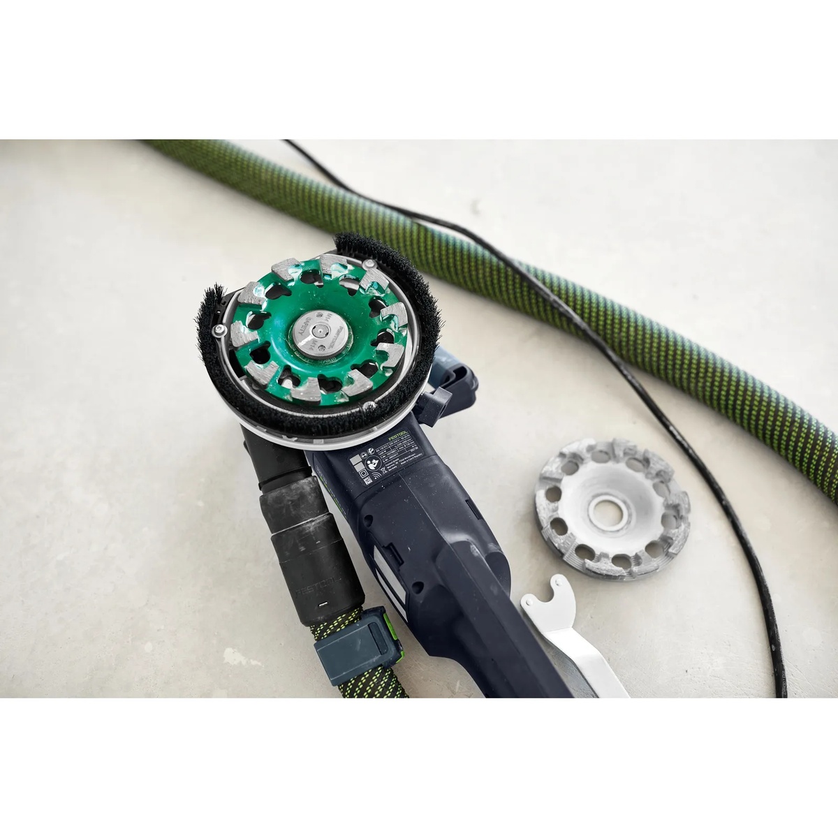 Festool 769166 DIA STONE-D130 PREMIUM Diamond Disc mounted on a Festool concrete grinder next to a removed wheel on a jobsite floor