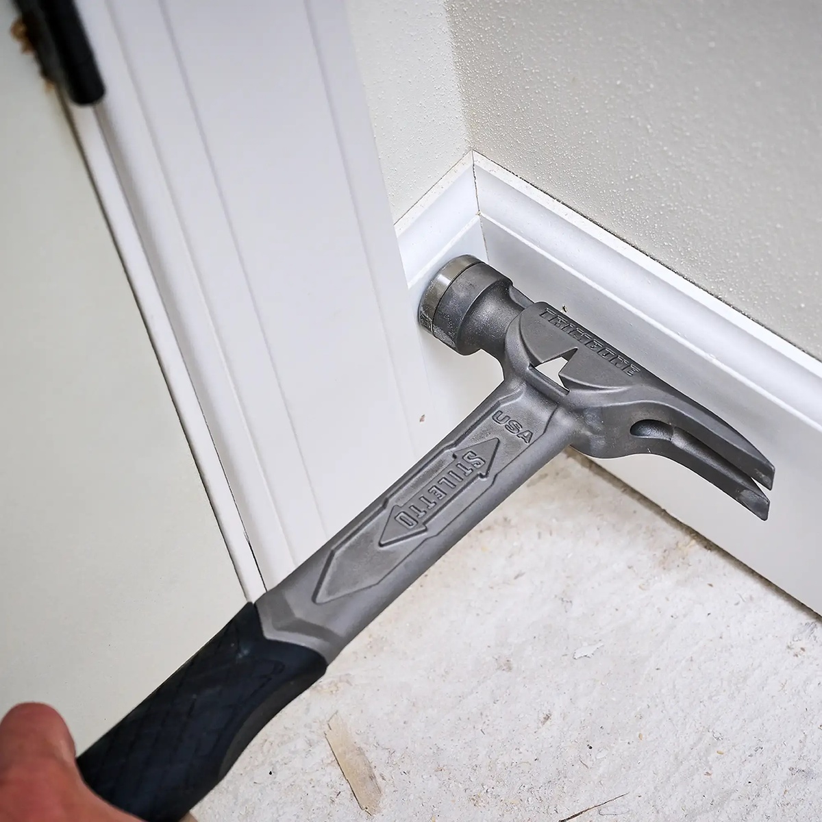 Stiletto TRIMBONE 10oz Titanium Finish Hammer using the claw to pull trim near a door jamb and baseboard during interior finish carpentry work