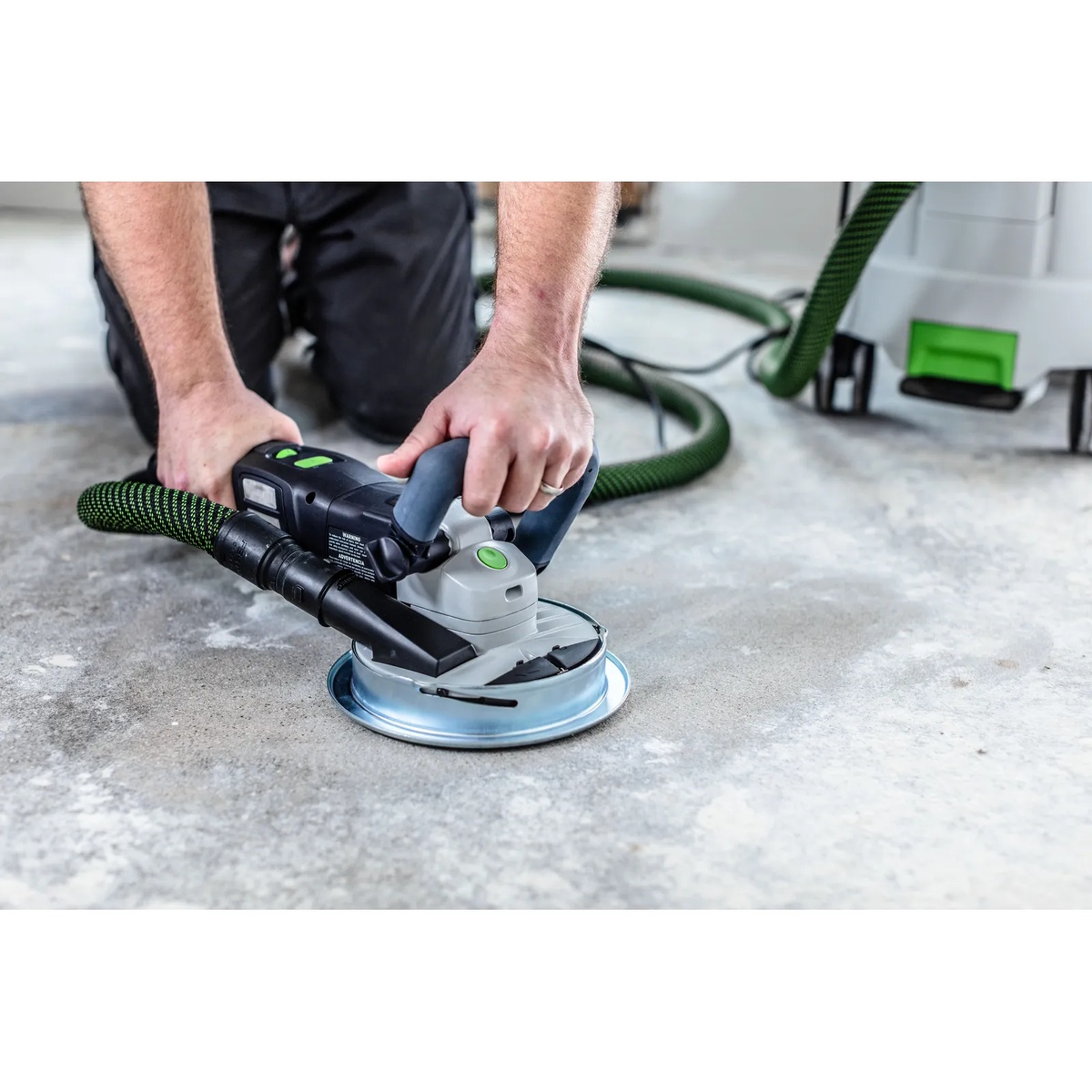 Festool 577048 Corded RENOFIX RG 130 ECI-Plus Surface Restoration Grinder Set connected to dust extraction while removing material from a concrete floor in a remodel setting