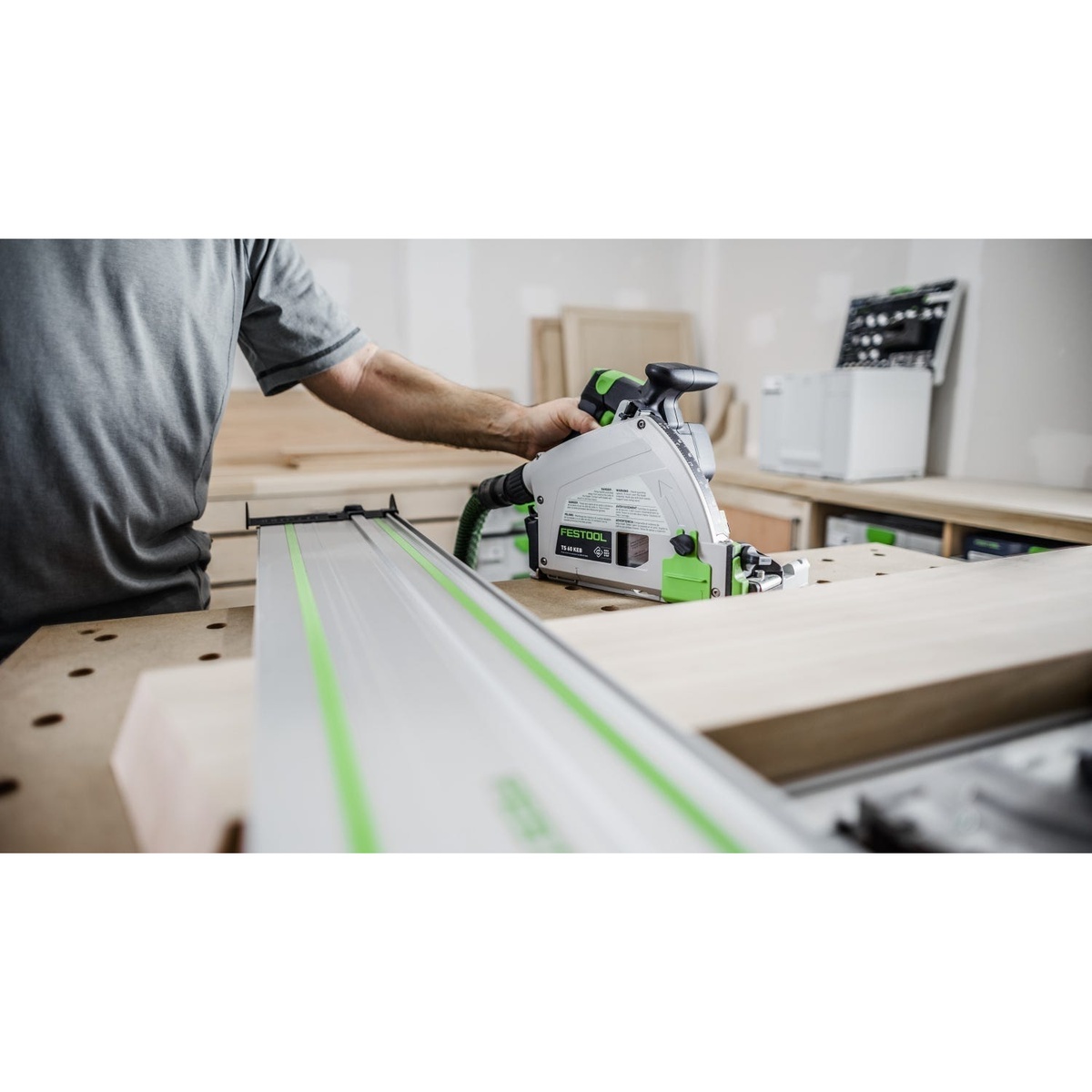Festool TS 60 KEB plunge cut track saw riding on a guide rail while trimming a wood panel on a workbench in a cabinet shop