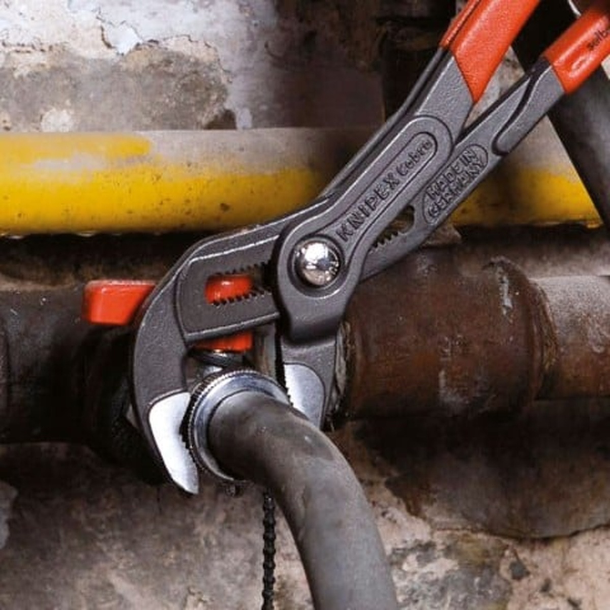Knipex 00 20 06 US1 3 Pc Cobra Pliers Set gripping a metal pipe fitting during plumbing repair work in a tight mechanical space