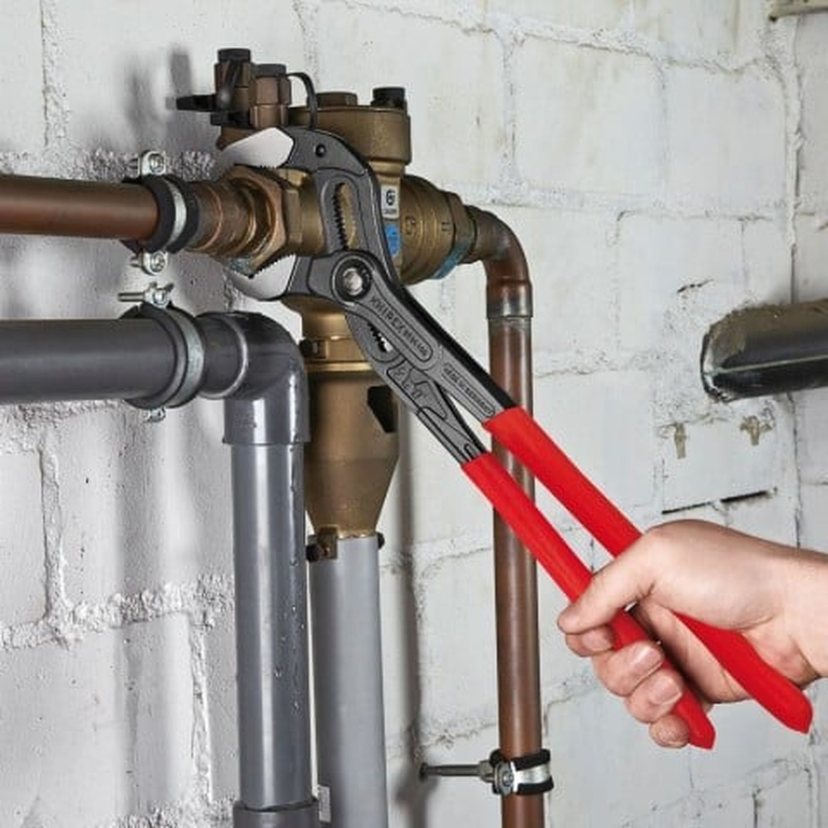 Knipex 87 01 400 US Cobra XL Water Pump Pliers gripping plumbing pipe and valve hardware on a wall-mounted mechanical line during service work