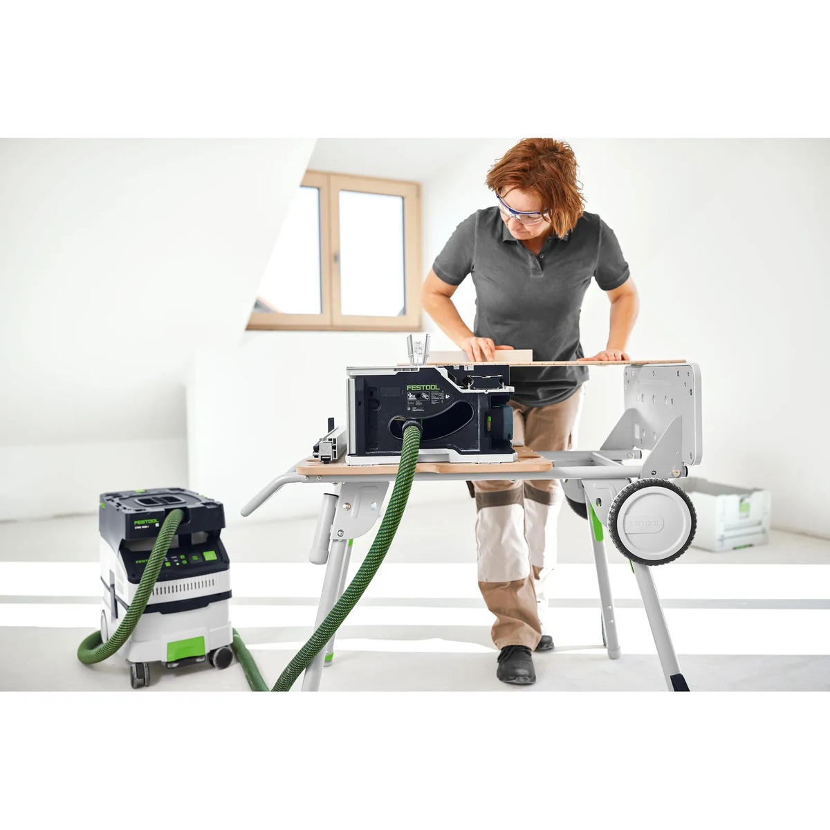 Festool 577001 CSC SYS 50 Cordless Table Saw Underframe UG UG-CSC-SYS supporting the CSC SYS 50 table saw during indoor cutting work with dust extraction attached