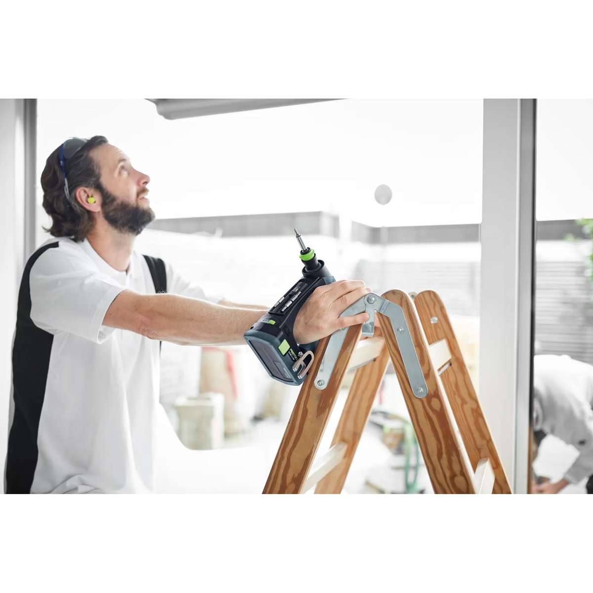 Festool 576887 CXS 18 BASIC Cordless Drill resting on a ladder during overhead fastening work on an interior jobsite