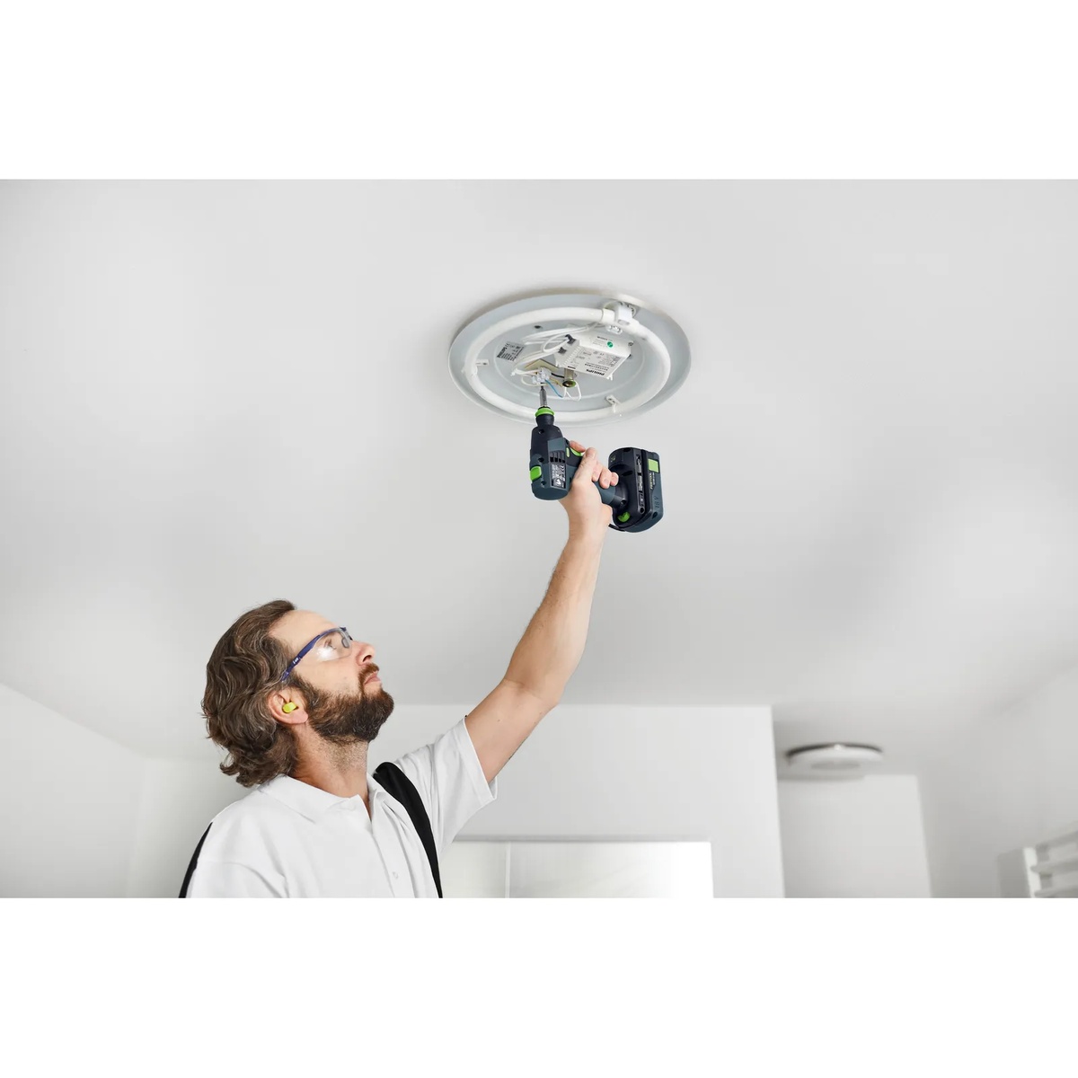 Festool TXS 18 BASIC Cordless Drill used overhead to fasten a ceiling light fixture during electrical installation work