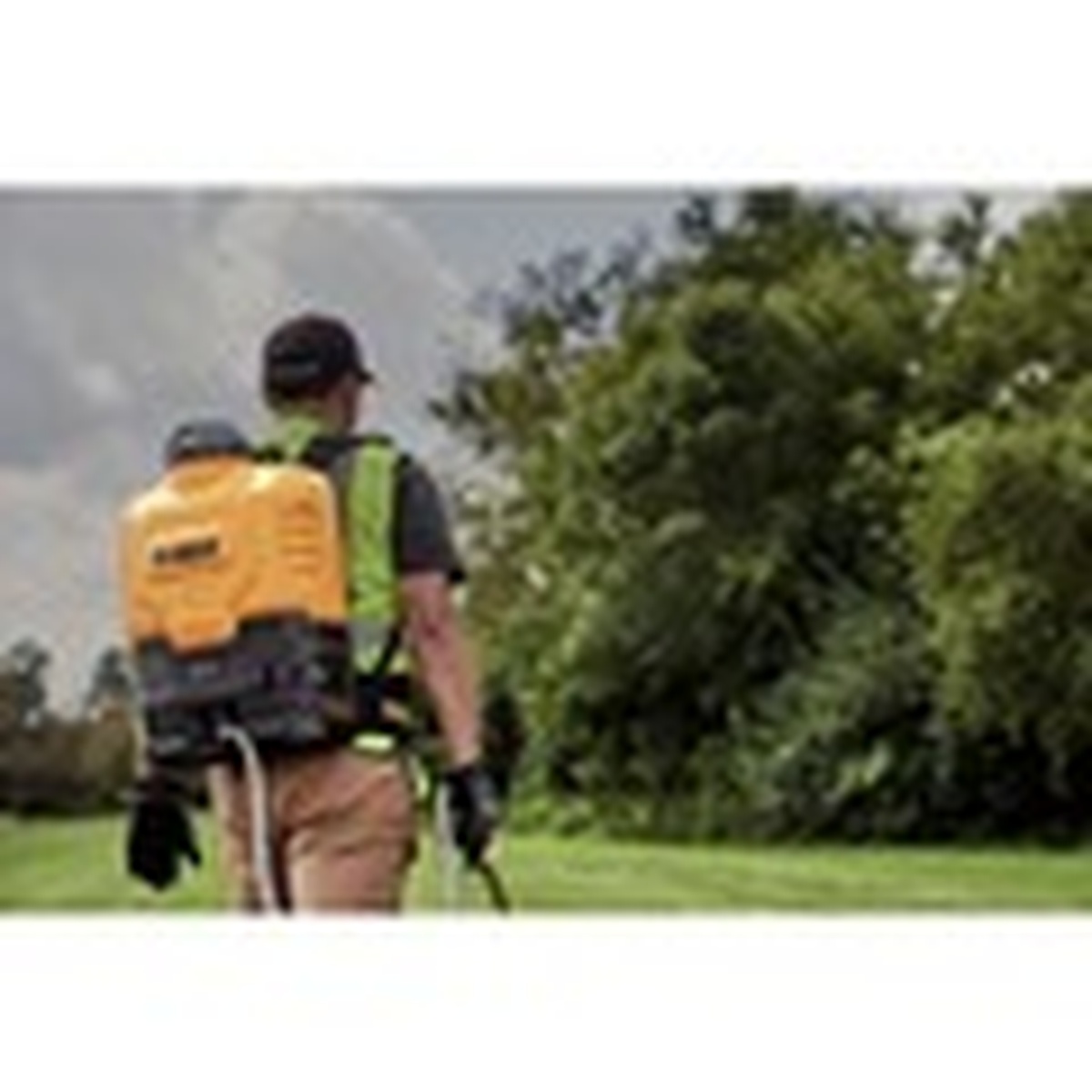 DeWalt DXSP190681B 20V MAX 4-Gallon Backpack Sprayer worn on a user walking a grassy property during outdoor spraying work