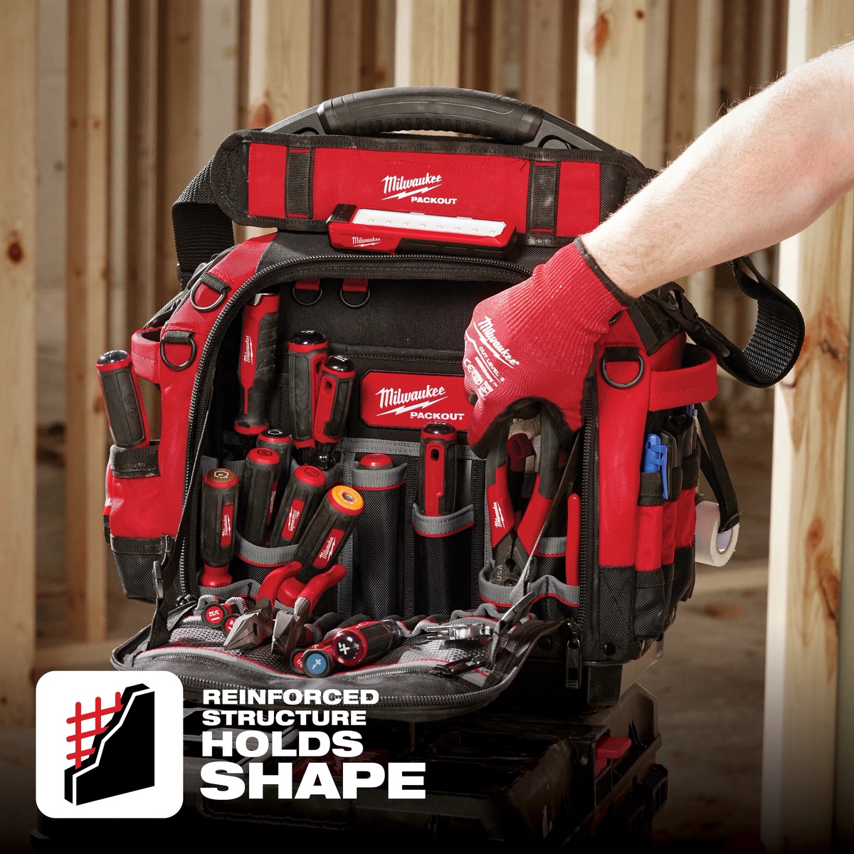 Milwaukee PACKOUT 15 in Structured Tool Bag opened on a framed jobsite wall, holding organized hand tools for electrical and service work