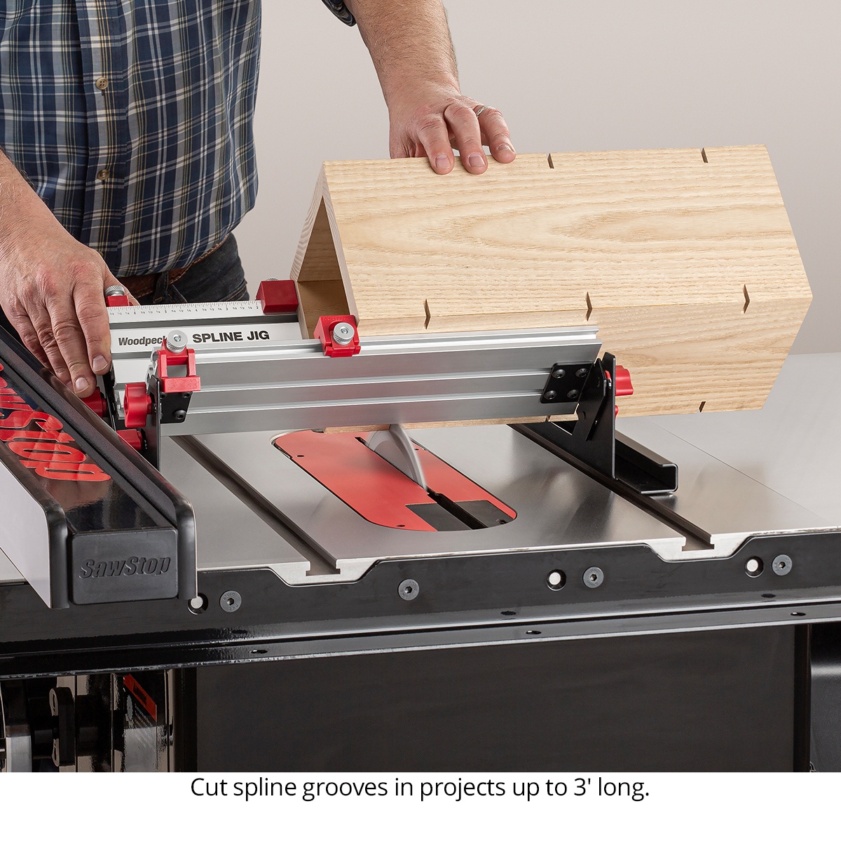 Woodpeckers Spline Jig guiding a long mitered wood assembly across a table saw blade while cutting spline grooves on a larger woodworking project