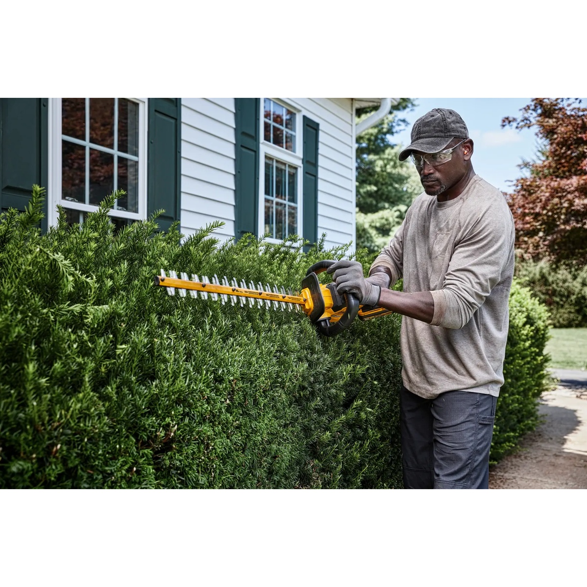 DEWALT 60V MAX 26-in. Brushless Cordless Hedge Trimmer shaping a hedge at chest height in a residential yard