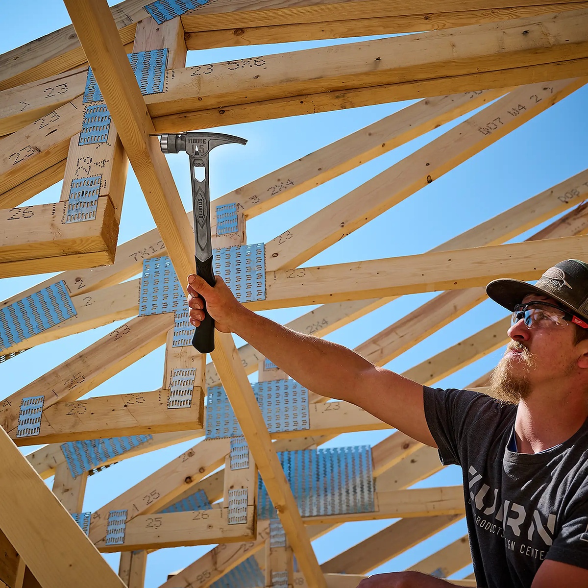 Stiletto TIBONE 15oz Smooth/Curved Titanium Framing Hammer held overhead during roof framing on a jobsite with wood trusses and framing connectors