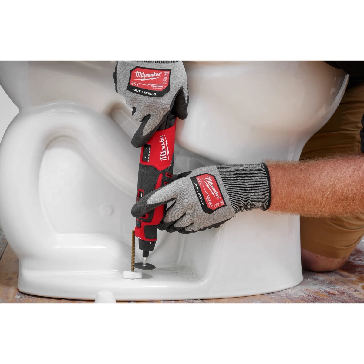 Milwaukee 2525-20 M12 Brushless Rotary Tool cutting hardware near the base of a toilet during bathroom installation work