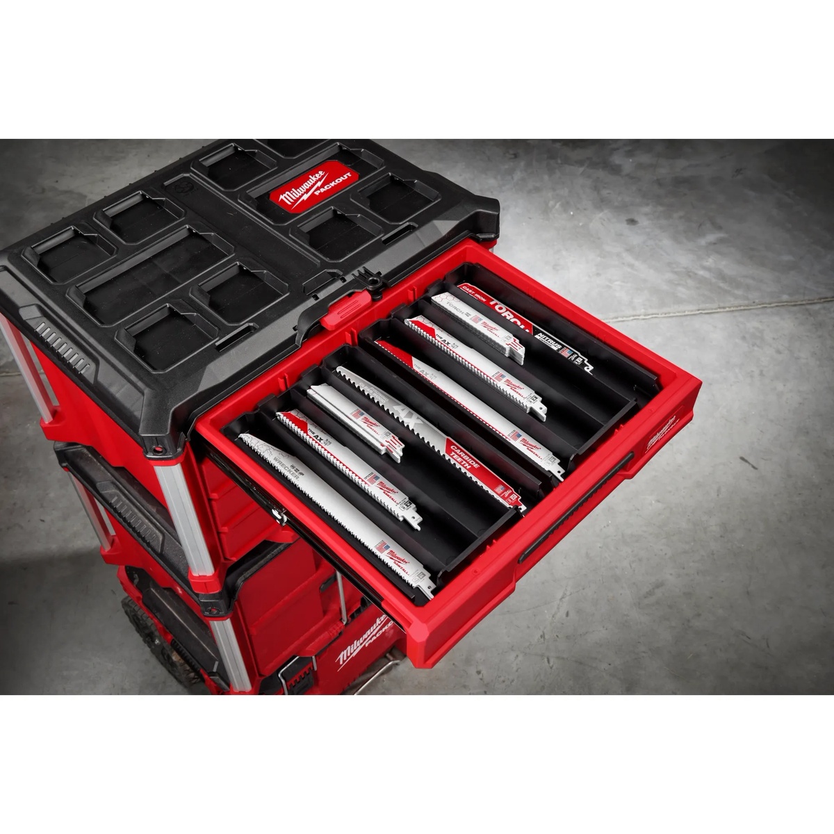 Milwaukee SAWZALL blade assortment stored in a removable tray inside a PACKOUT drawer, showing multiple reciprocating saw blade lengths and tooth styles for wood cutting and metal cutting