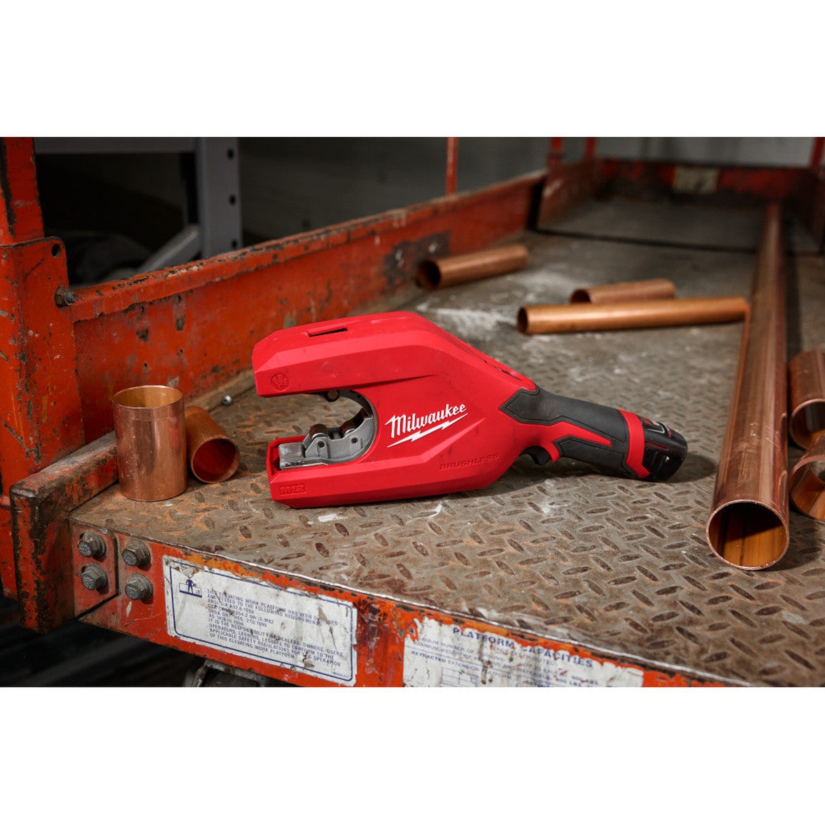 Milwaukee 2479-20 M12 Brushless 1-1/4 inch to 2 inch Copper Tubing Cutter on a jobsite platform beside large copper tubing for plumbing and mechanical installation work