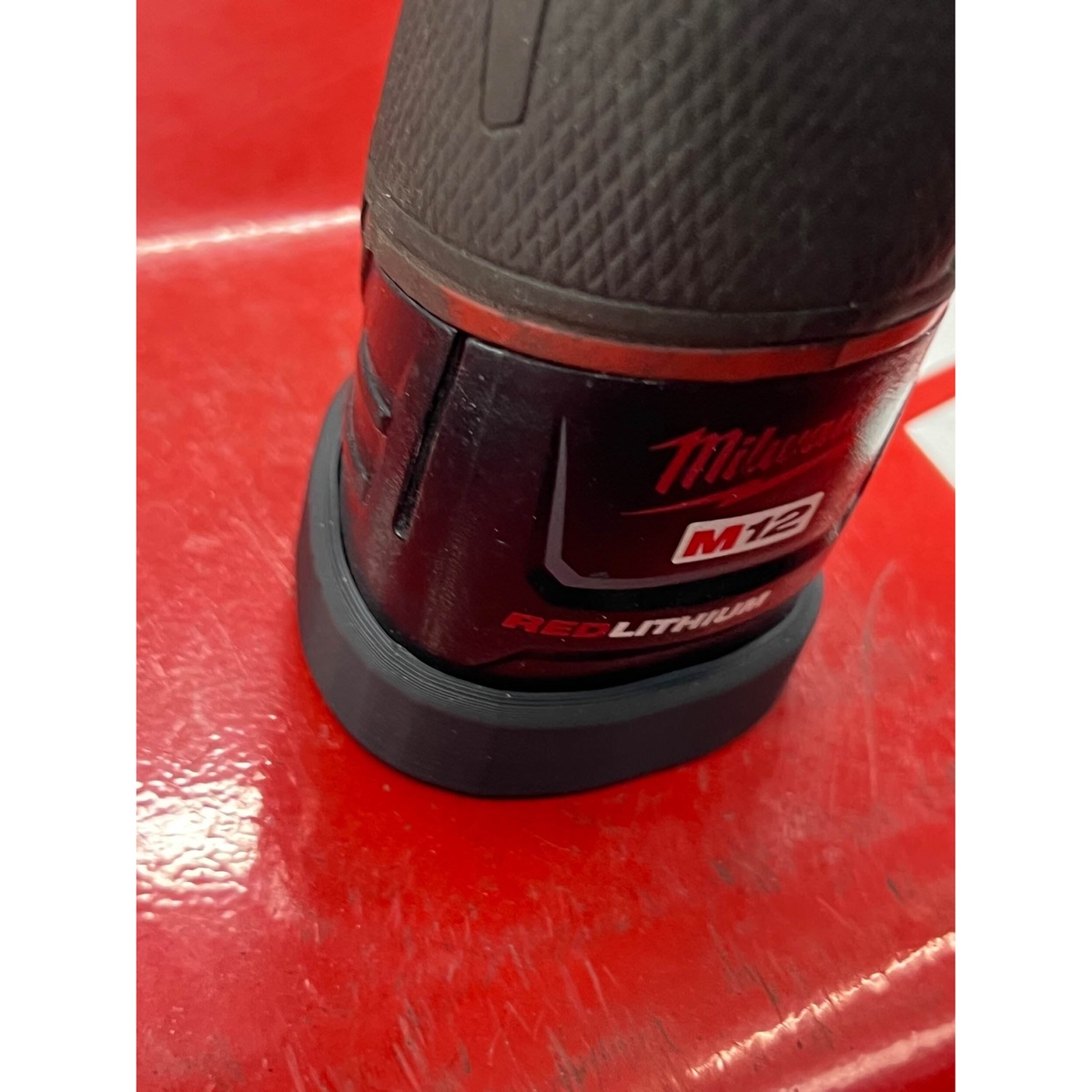 close-up of STS Auto Design MW12TL Milwaukee M12 Tri-Lobe Magnet Battery Cover fitted to a Milwaukee M12 battery on a red steel work surface
