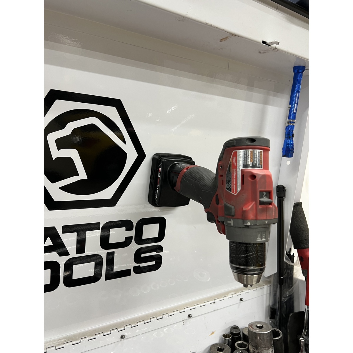 STS Auto Design MW12XC Milwaukee M12 XC Magnetic Battery Cover mounted on a metal tool cabinet holding an M12 tool battery in a real shop storage setup