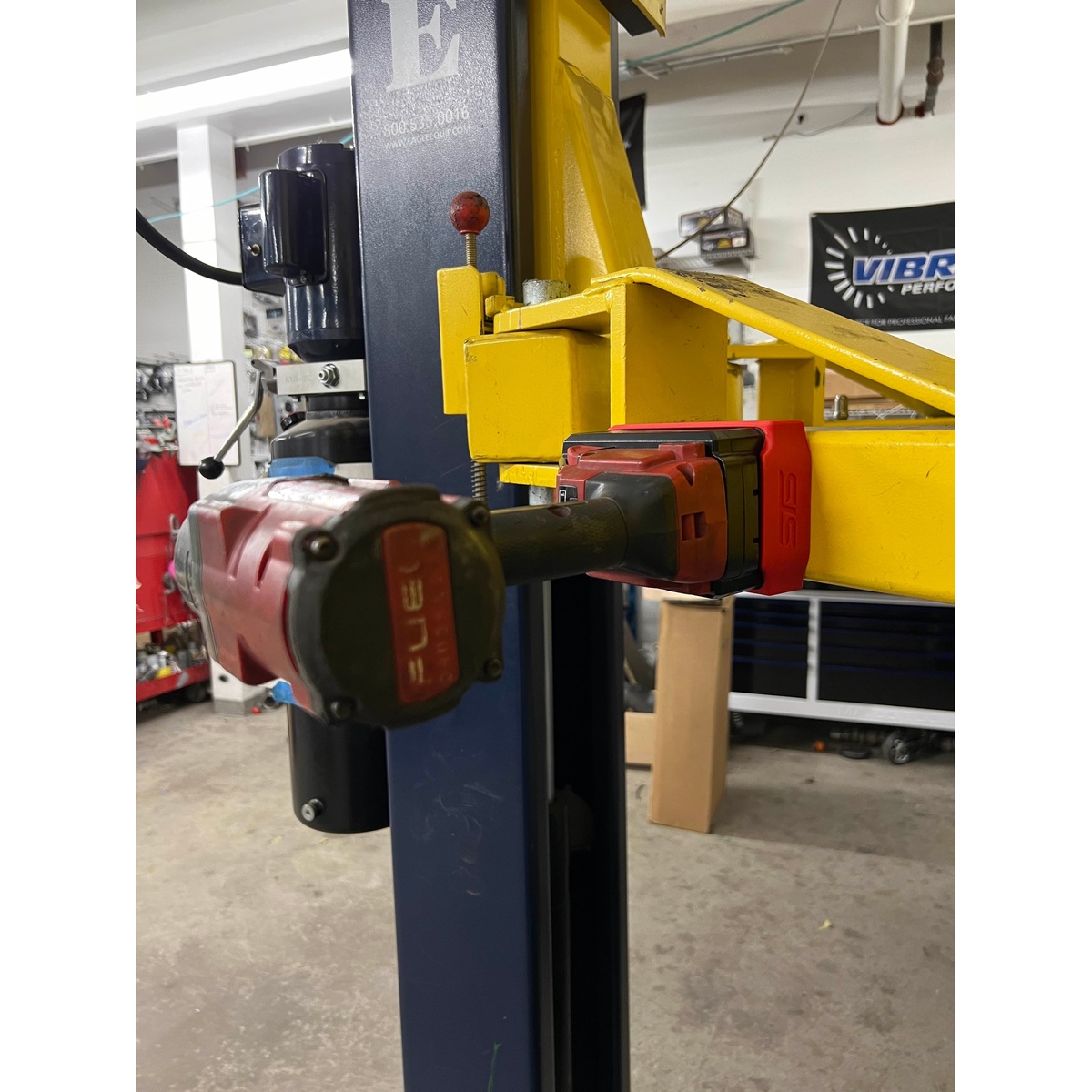 STS Auto Design M18H6 Milwaukee M18 Hi-Output 6.0Ah 8.0Ah Magnetic Battery Cover holding a cordless tool on a steel shop lift in a garage workspace