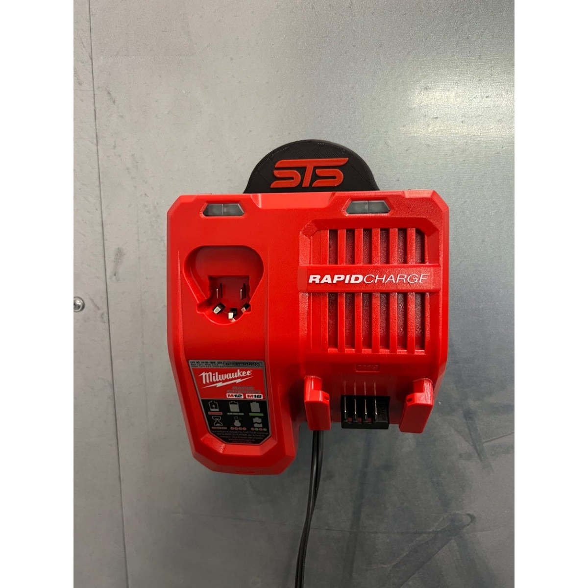 STS Auto Design M1218RC Milwaukee M12/M18 Rapid Charger Magnetic Holder mounted on a steel wall with a Milwaukee rapid charger installed in a workshop charging setup