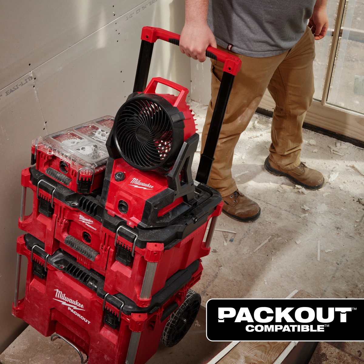 Milwaukee M18 Brushless PACKOUT Fan mounted on PACKOUT storage being rolled through an indoor remodeling jobsite for portable personal cooling