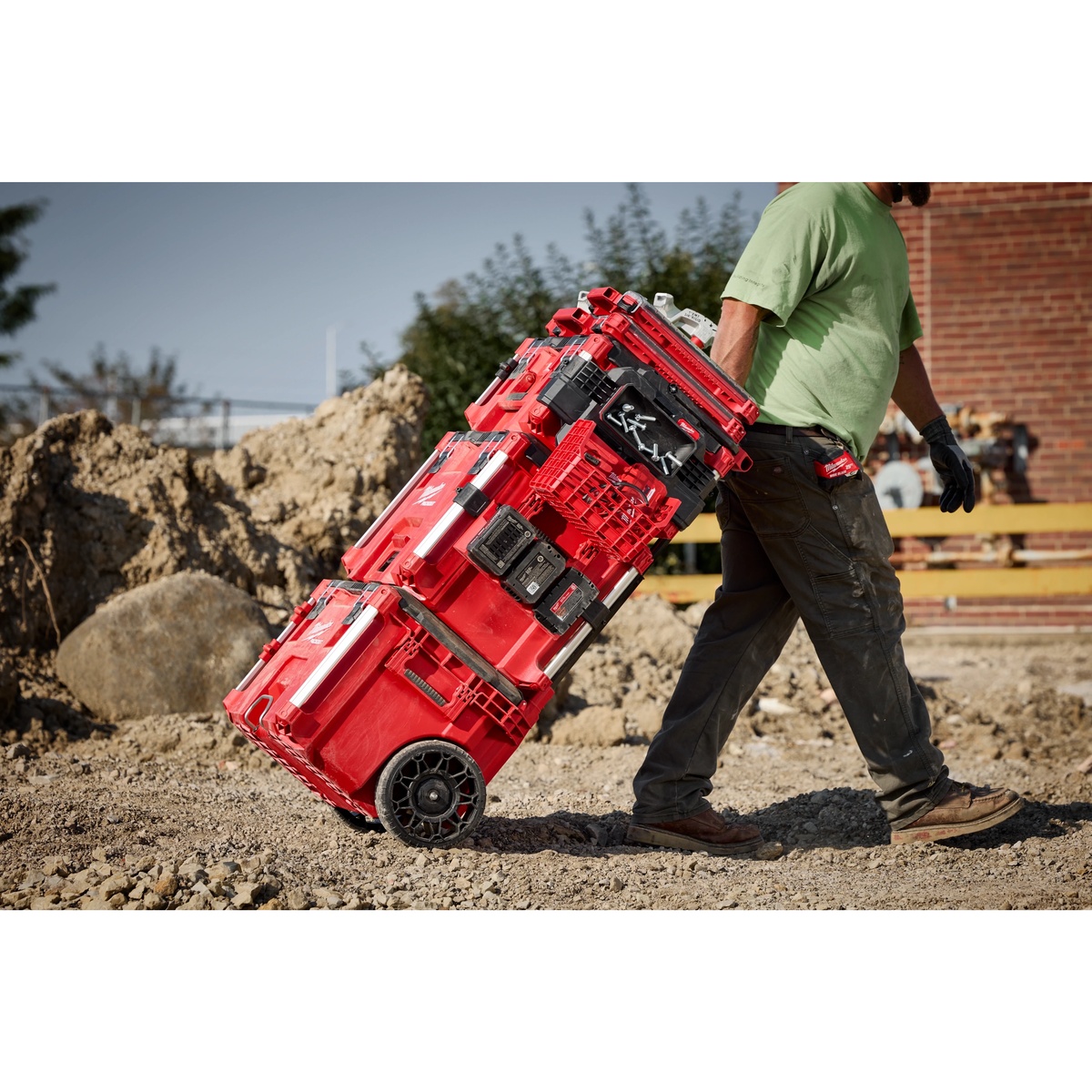 Milwaukee PACKOUT Rolling Tool Box 48-22-8427 being pulled across rough dirt on a jobsite with stacked PACKOUT cases loaded on top