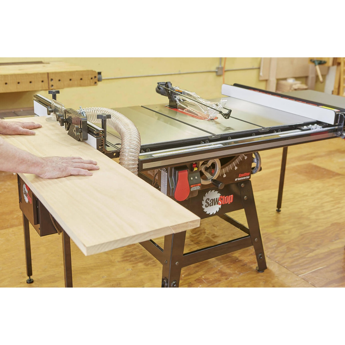 SawStop CNS175-PFA30 Contractor Saw ripping a wide wood panel in a workshop with fence, blade guard, and dust hose connected for shop woodworking