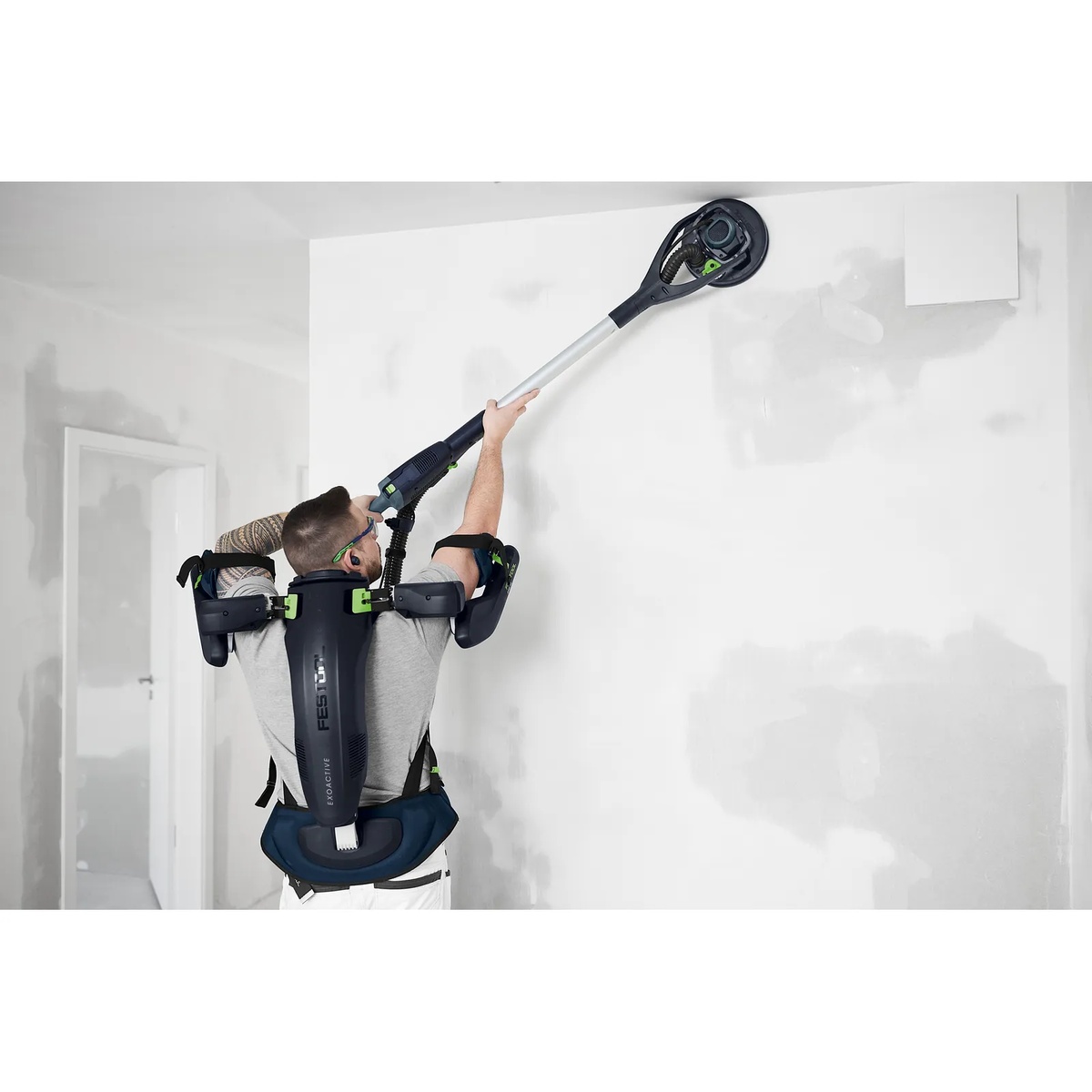 Festool EXO 18 HPC 4.0 I-Plus ExoActive Exoskeleton supporting a drywall finisher using a long-reach sander on an interior wall and ceiling during overhead sanding work