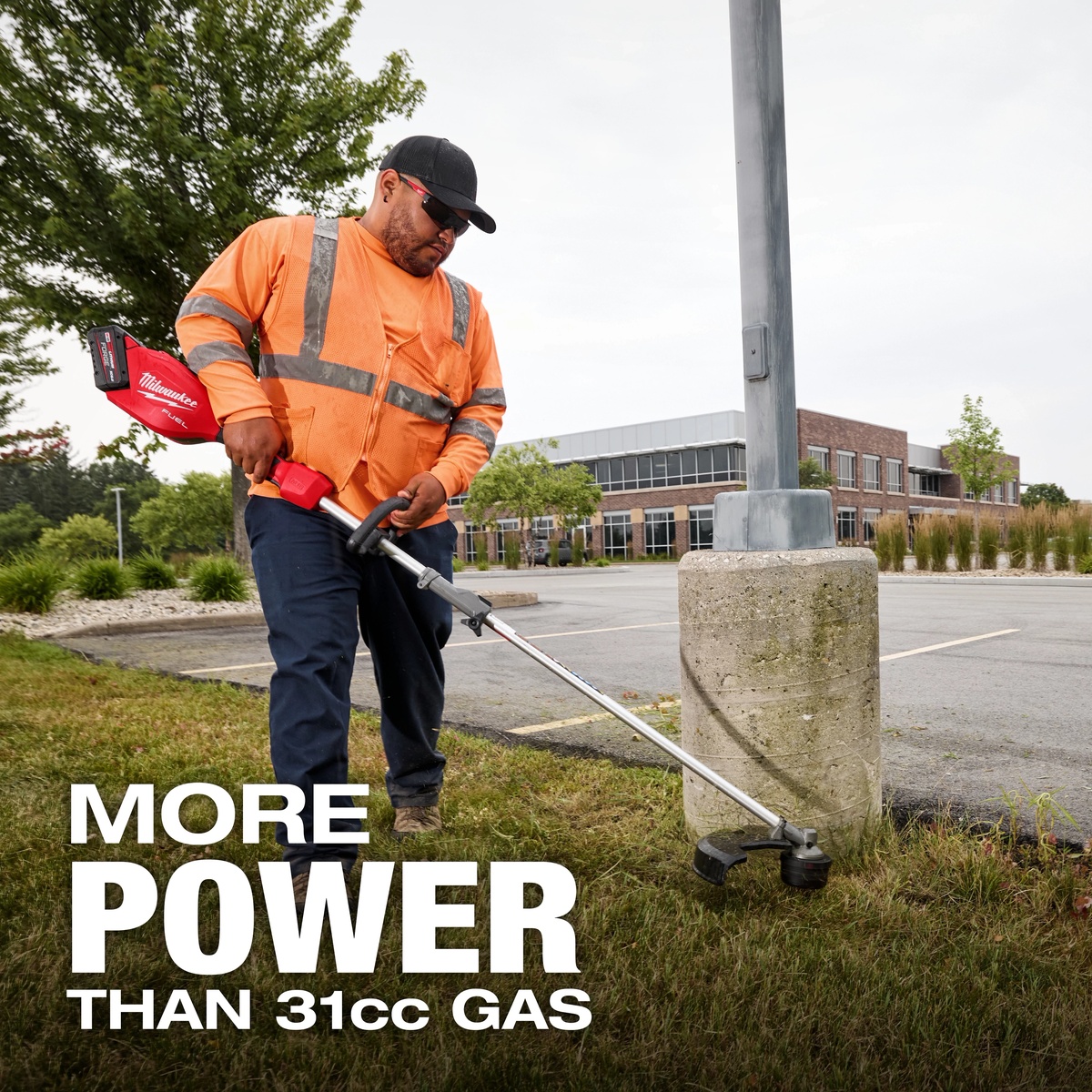Milwaukee M18 FUEL Power Head w/ QUIK-LOK being used with a string trimmer attachment to cut grass around a concrete light pole in a commercial parking lot