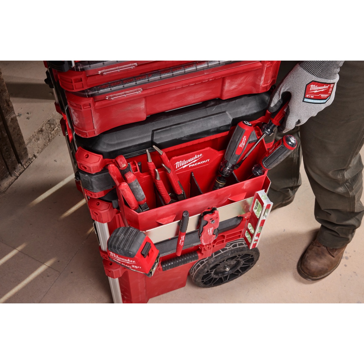 Milwaukee PACKOUT Tool Box Caddy Attachment mounted on a PACKOUT rolling tool box holding screwdrivers, hand tools, tape measure, and layout tools during interior jobsite work