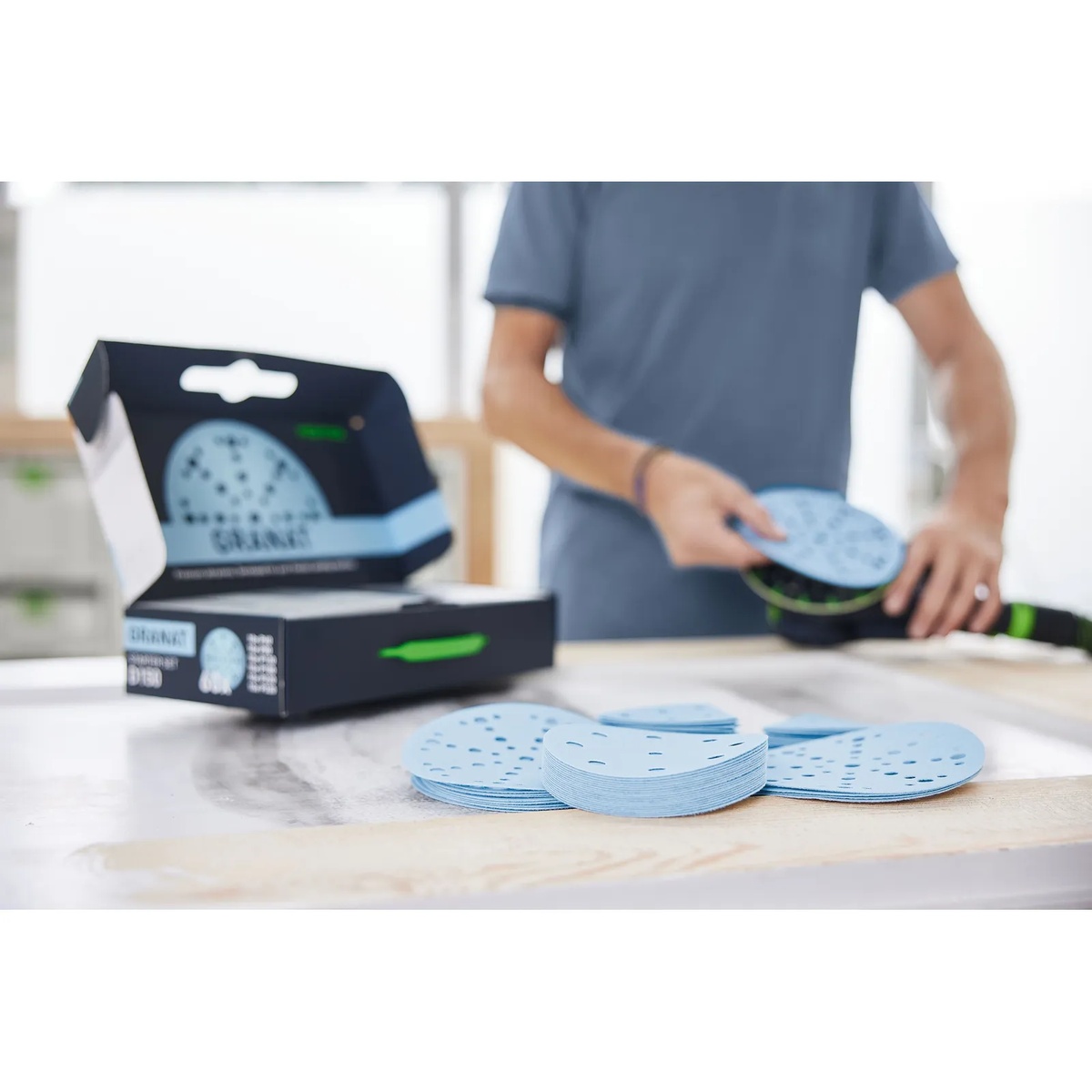 Festool Granat 6 inch sanding discs from the starter set stacked on a bench while being fitted to a Festool sander for dust-controlled sanding in a shop