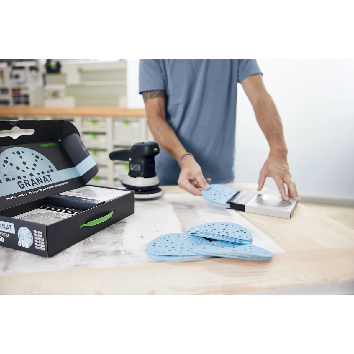 Festool 578166 D150 6-Inch Granat Abrasives 60/80/120/180/220/320-Grit 60-Piece Starter Set discs laid out on a workbench beside a Festool sander during surface preparation in a workshop