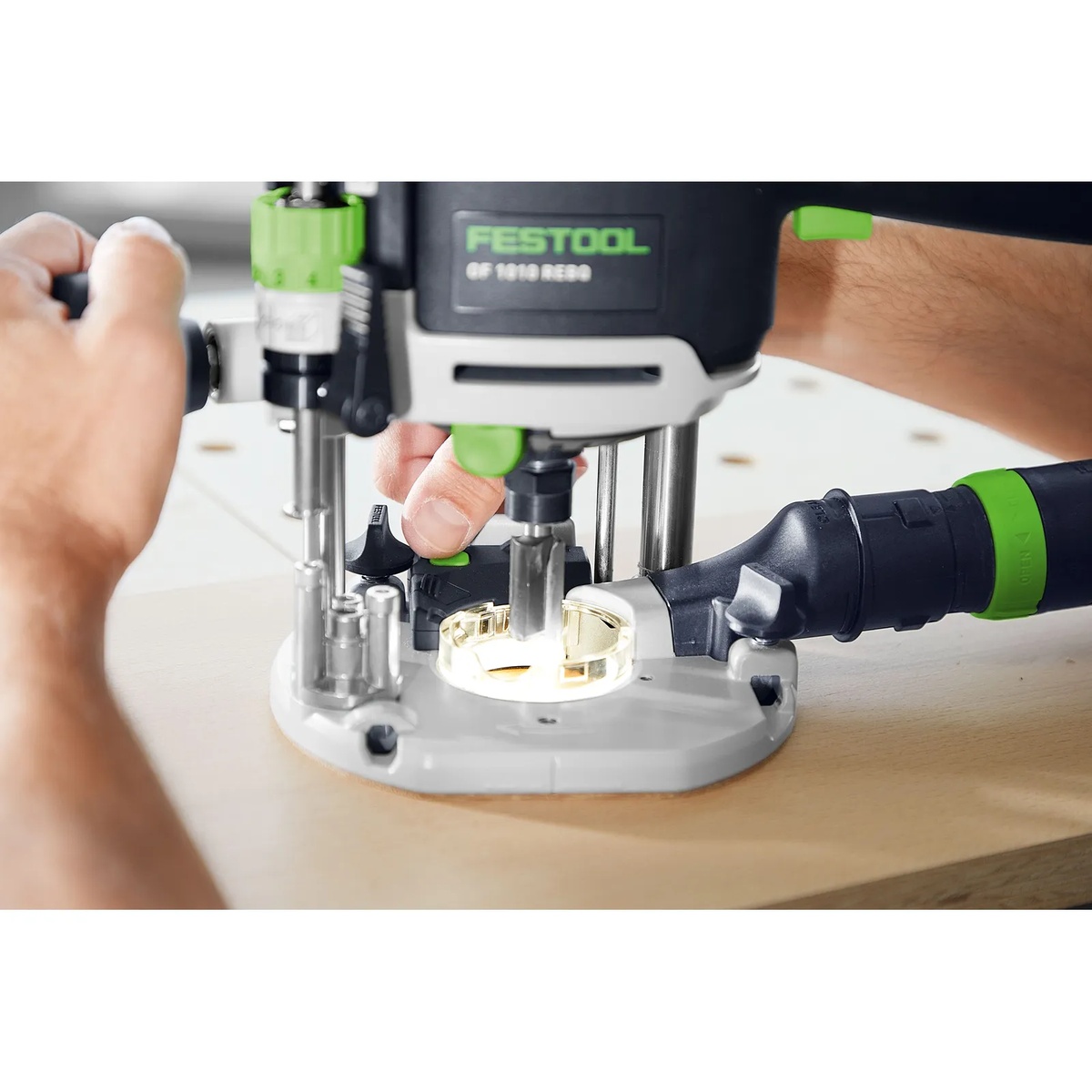 Festool OF 1010 REBQ-Plus Router cutting into a wood panel with the integrated LED light ring illuminating the routing area for precise work in a cabinet or bench setup