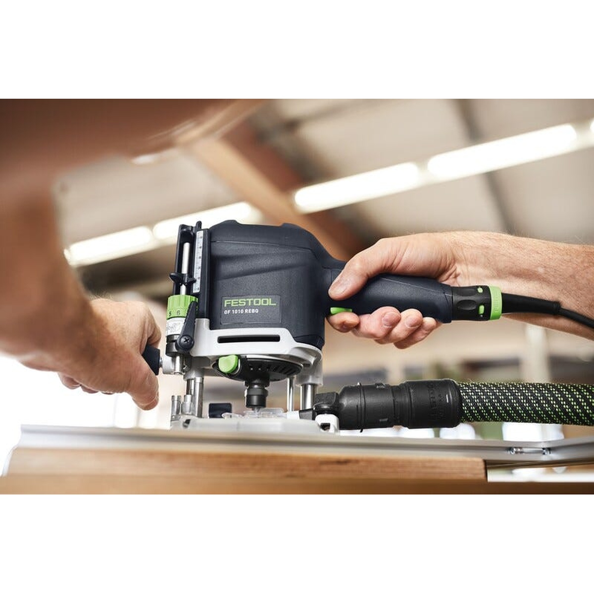 Festool 578307 OF 1010 REBQ-Set Router w/ ZS-OF 1010 I Accessory Set routing wood on a workbench with dust hose attached in a woodworking shop